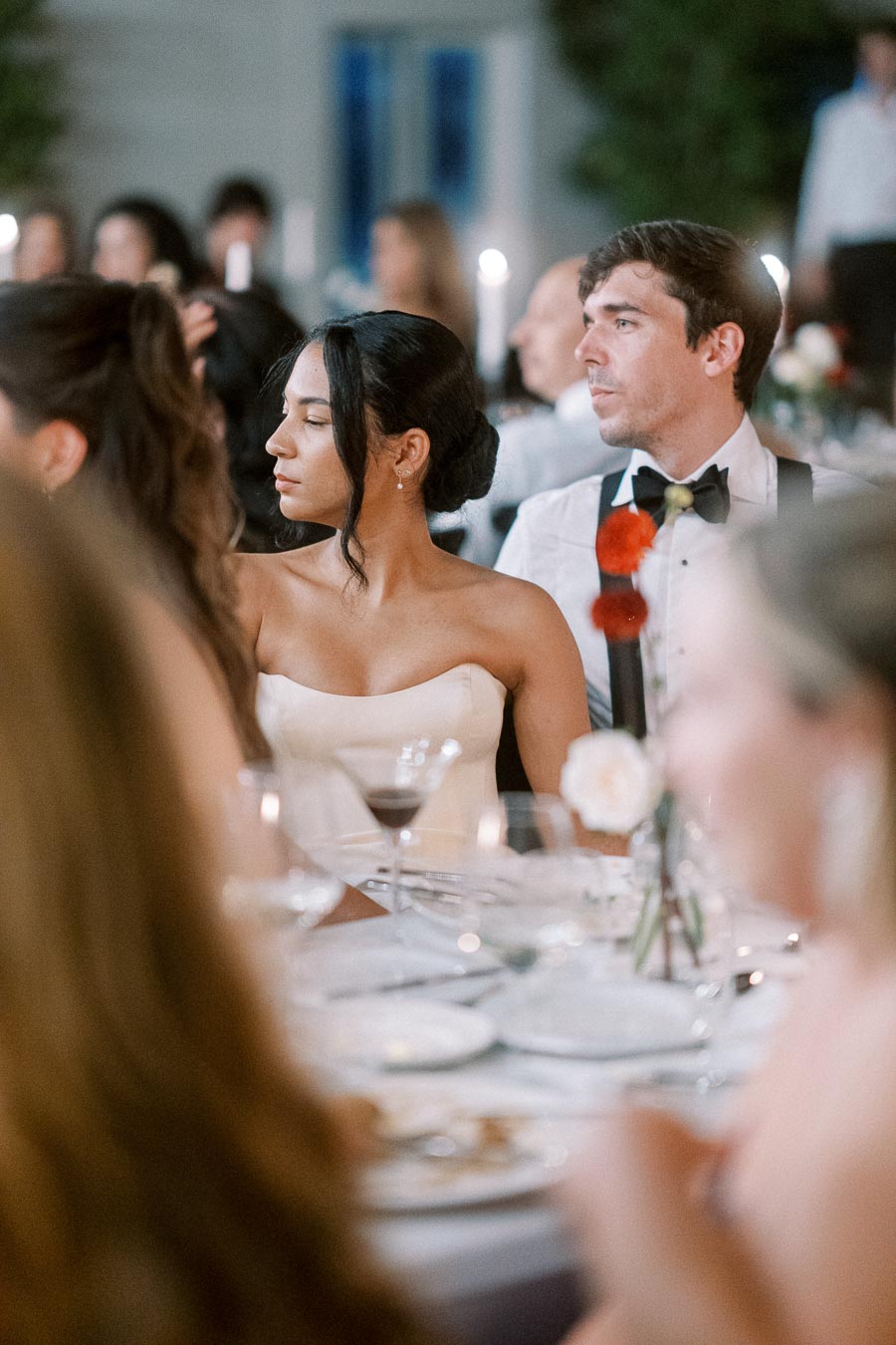 Elegant wedding guests seated at a beautifully set table, focusing on a well-dressed couple engaged in the celebration, with soft candlelight adding ambiance.