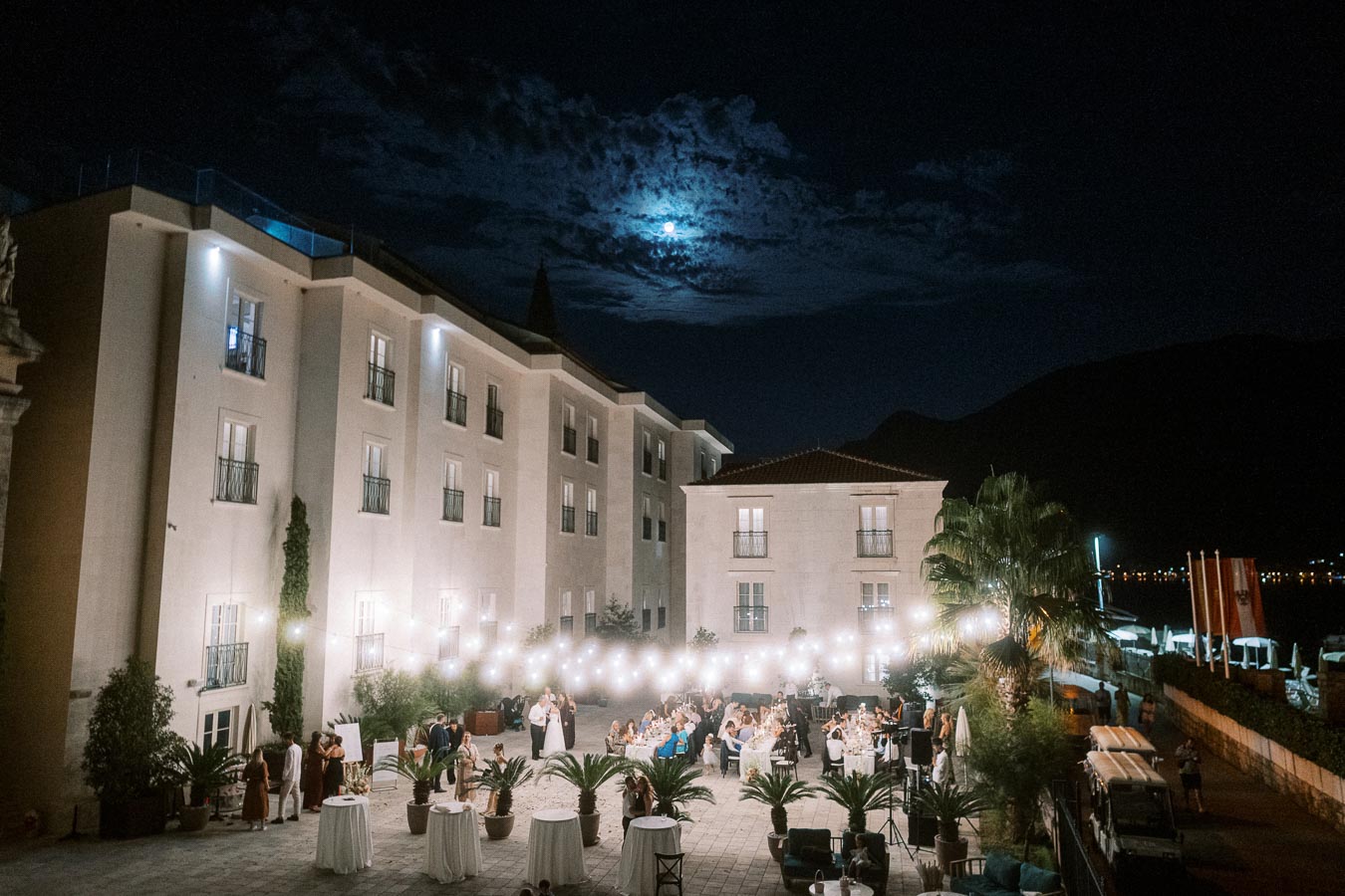 Elegant outdoor evening wedding reception with string lights at a luxury hotel courtyard under a moonlit sky.