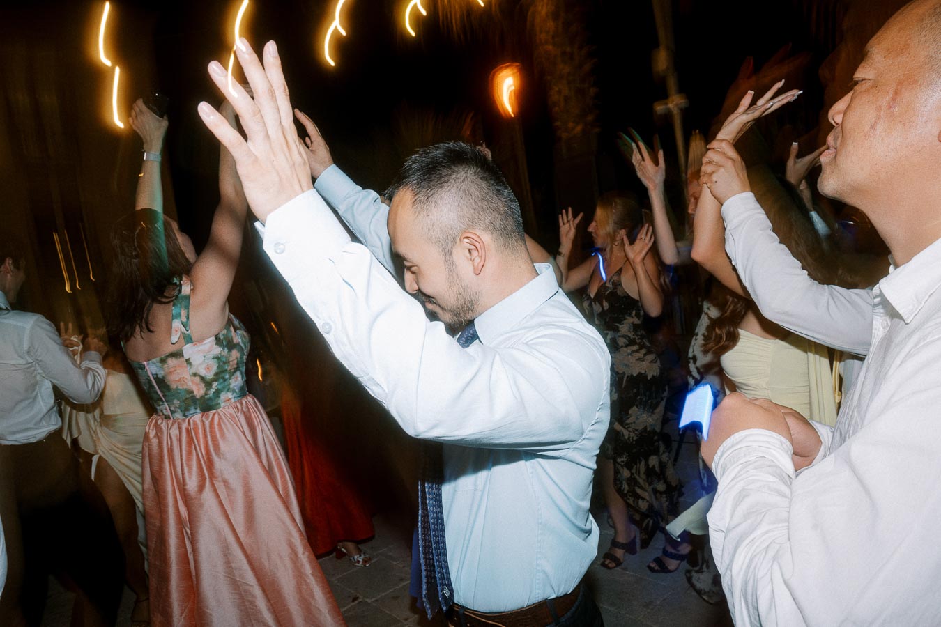 People joyfully dancing at a lively celebration with vibrant party lights and festive attire.
