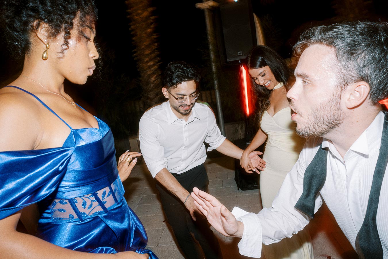A group of people enjoying an evening dance party, with a woman in a blue dress and a man in a vest prominently featured, capturing a lively and joyful atmosphere.