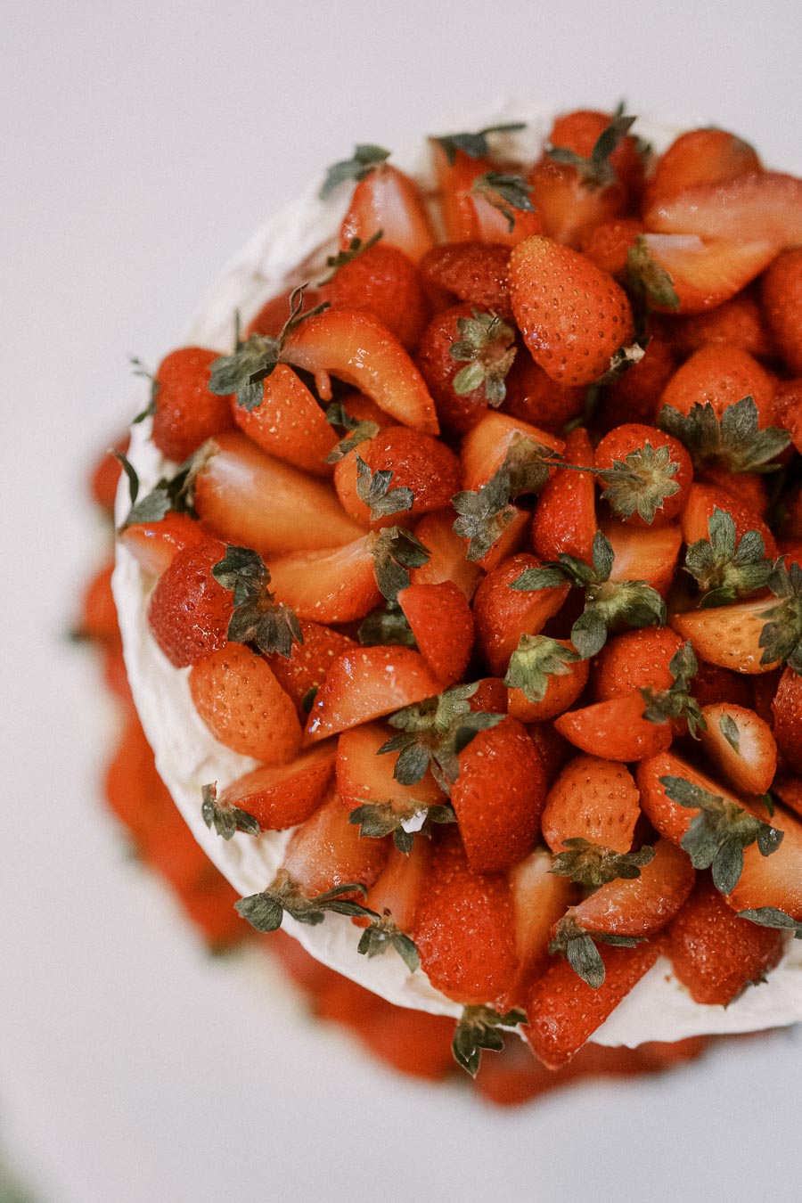 Top view of a cake garnished with fresh, sliced strawberries and white cream frosting.