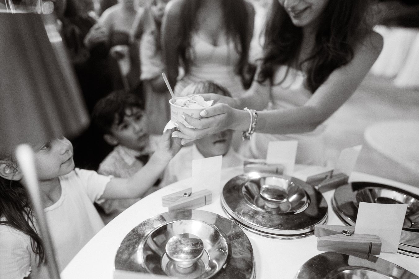 Black and white photo of children reaching for ice cream being served by a woman at a dessert counter during a social event.