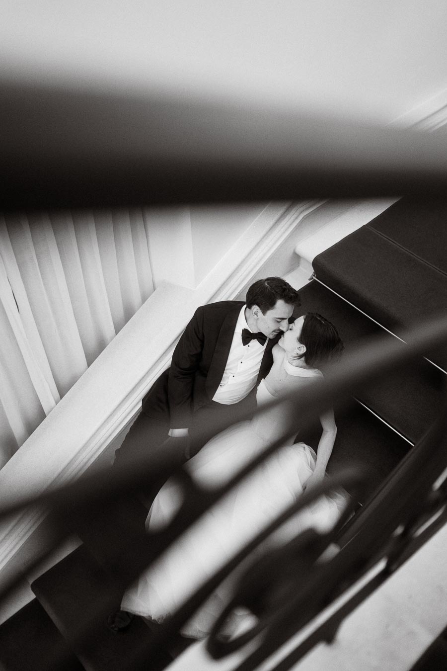 Black and white photo of a bride and groom sharing a kiss on a staircase, with a romantic and intimate ambiance.