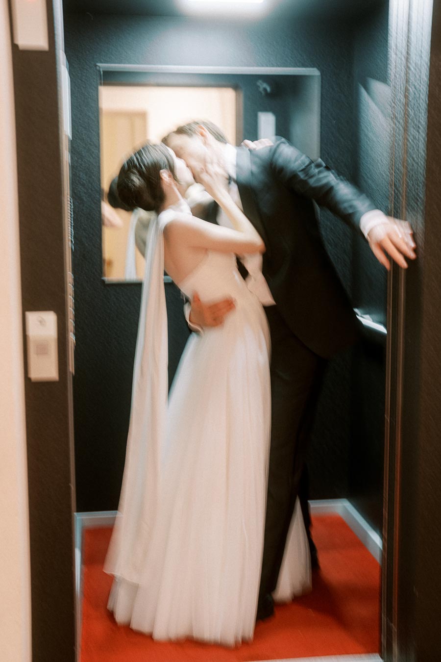 Romantic moment captured as a bride and groom share a kiss in an elevator, highlighting wedding day joy and elegance.