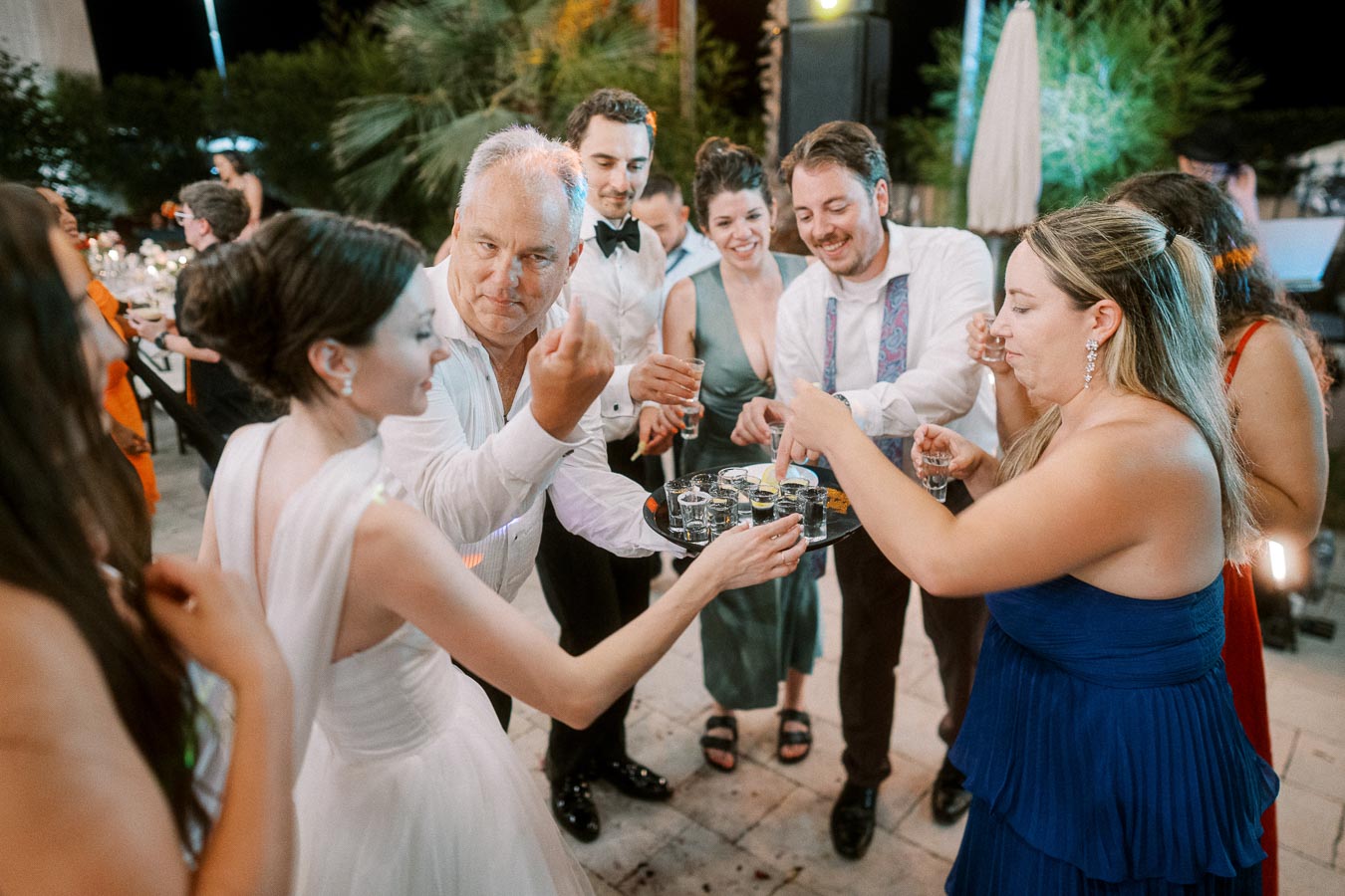 Group of people enjoying a festive celebration outdoors at night, with partygoers holding drinks and smiling.