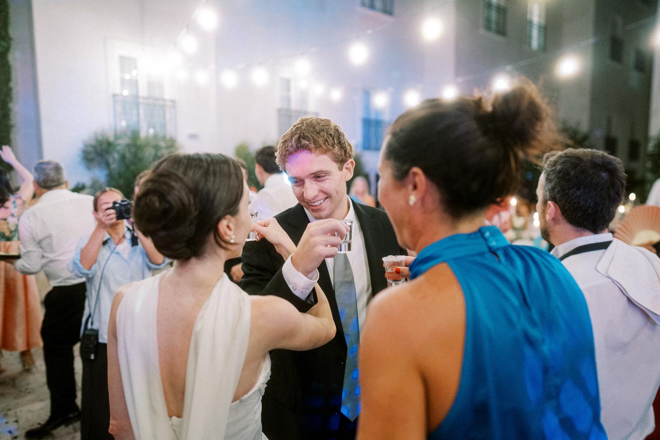Wedding reception celebration with guests toasting under string lights, capturing a joyful moment of friends and family enjoying an outdoor evening event.