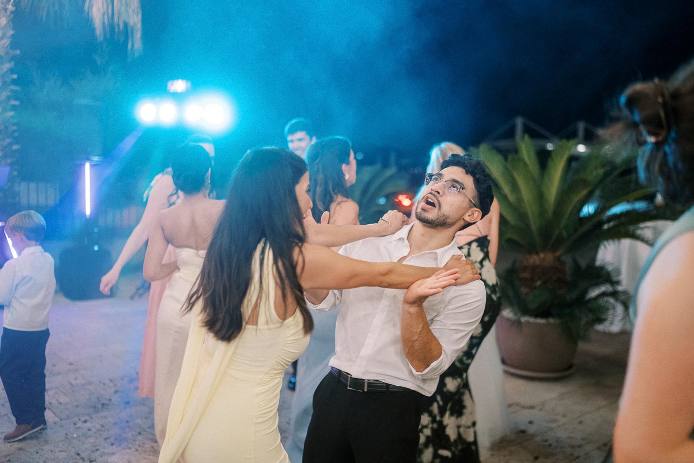 A lively wedding reception dance floor with guests in formal attire celebrating under colorful lights.