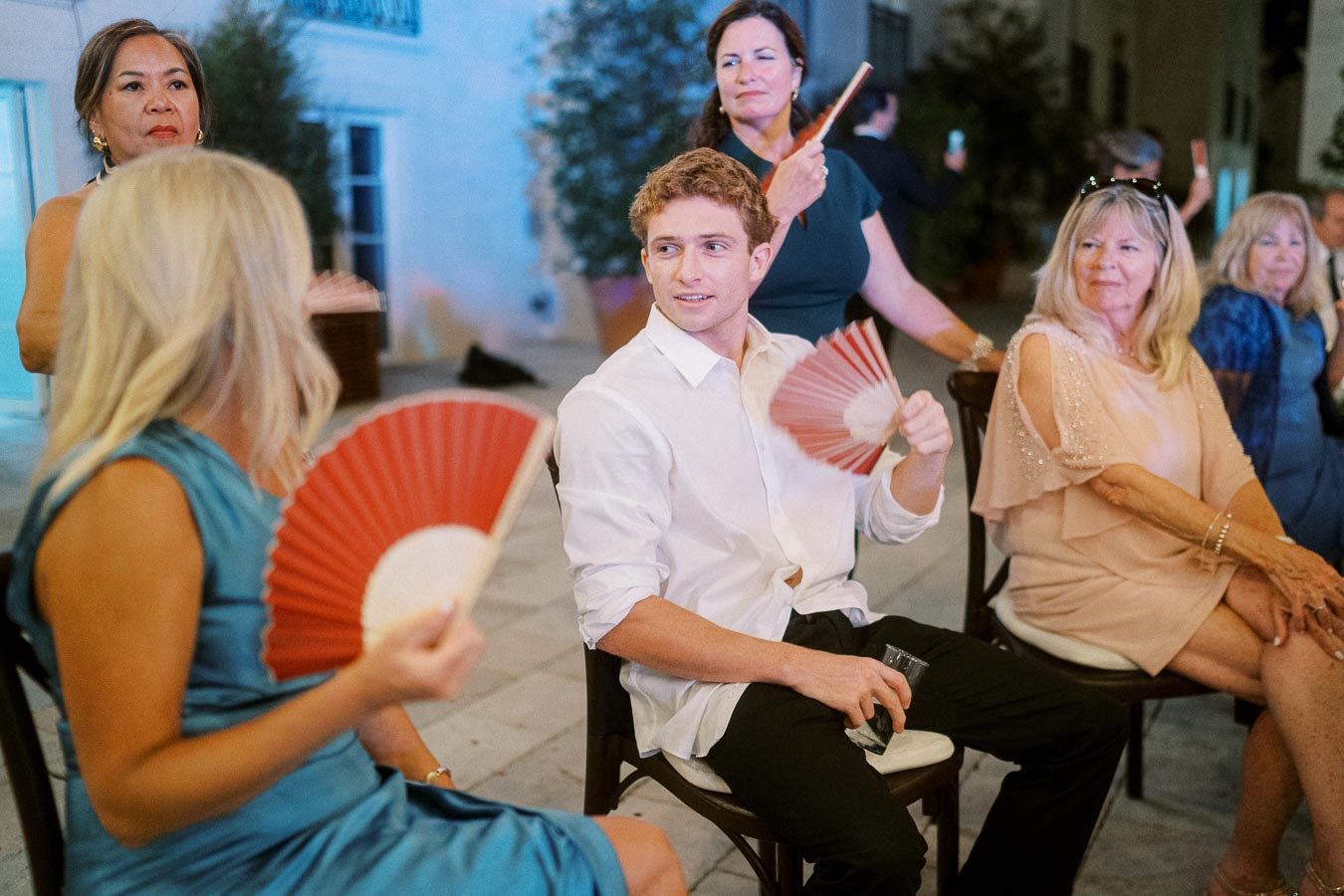 People at a social gathering enjoying themselves with decorative fans while sitting and interacting.