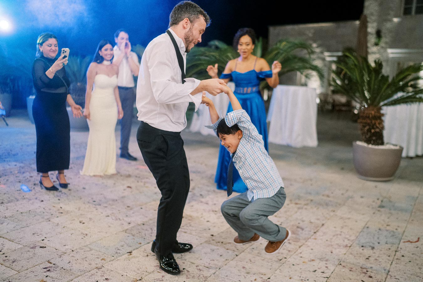 A joyful wedding dance celebration with a man and child having fun on the dance floor, surrounded by guests in elegant attire, creating a lively and festive atmosphere.