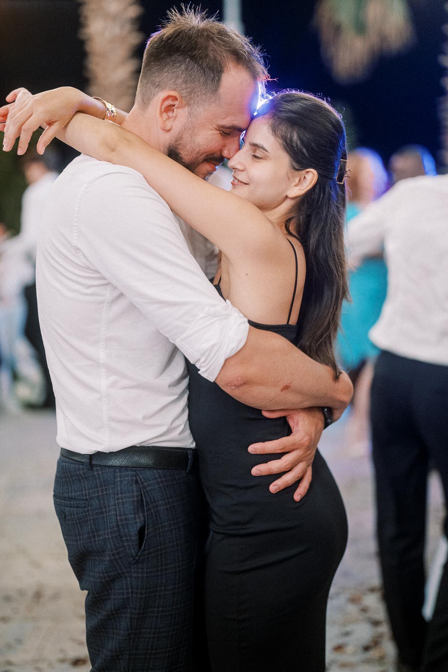 A couple embracing and smiling while dancing outdoors at night, surrounded by a softly lit background.