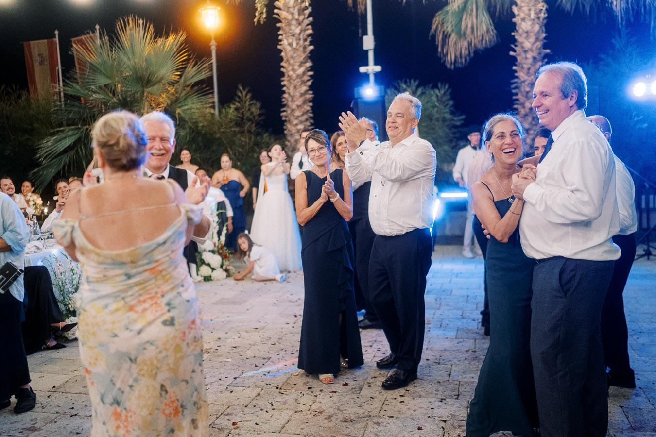 A lively wedding reception with guests dancing and applauding under string lights, creating a joyful and festive atmosphere.
