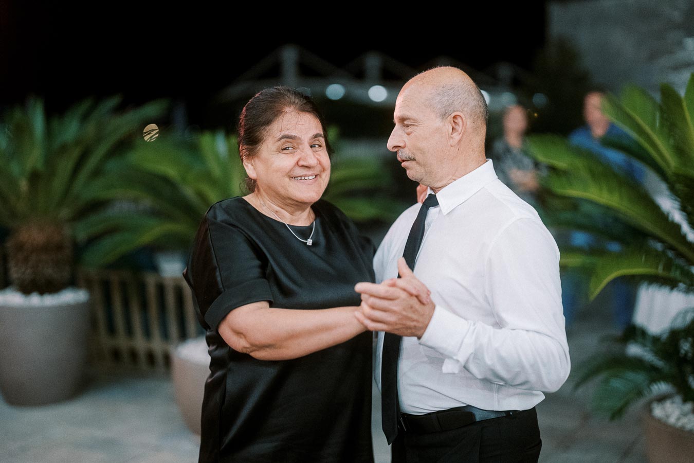 Elderly couple dancing joyfully outdoors at night, surrounded by lush greenery.