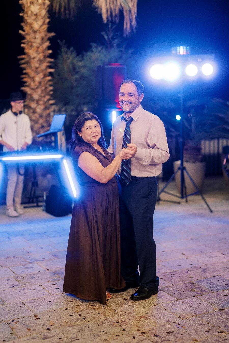 A couple dancing joyfully under bright lights at an outdoor evening event, with a DJ in the background.