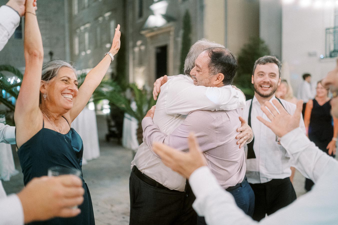 A group of joyous people celebrating at an outdoor event, with two men embracing, a woman raising her arms in happiness, and others smiling around them.