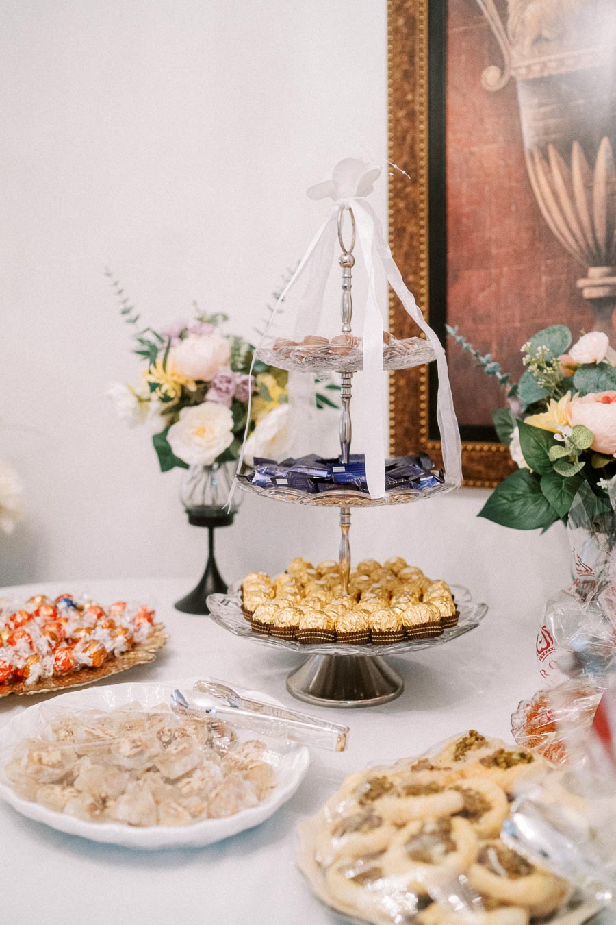 Elegant dessert table with a three-tier stand displaying assorted chocolates, surrounded by plates of cookies and sweets,