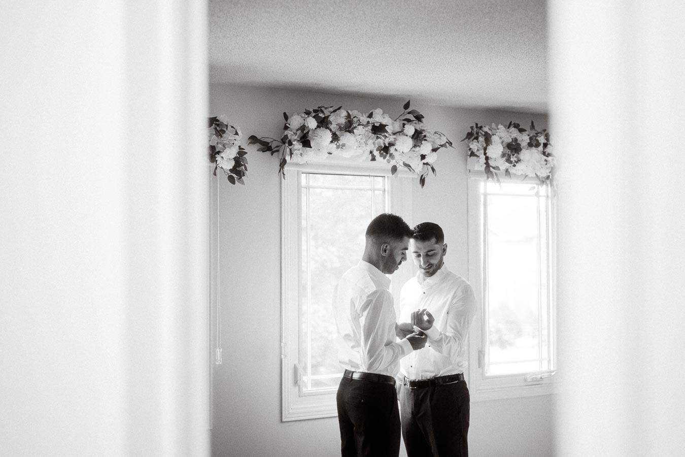A black and white photo of two elegantly dressed individuals in a room decorated with floral arrangements, thoughtfully