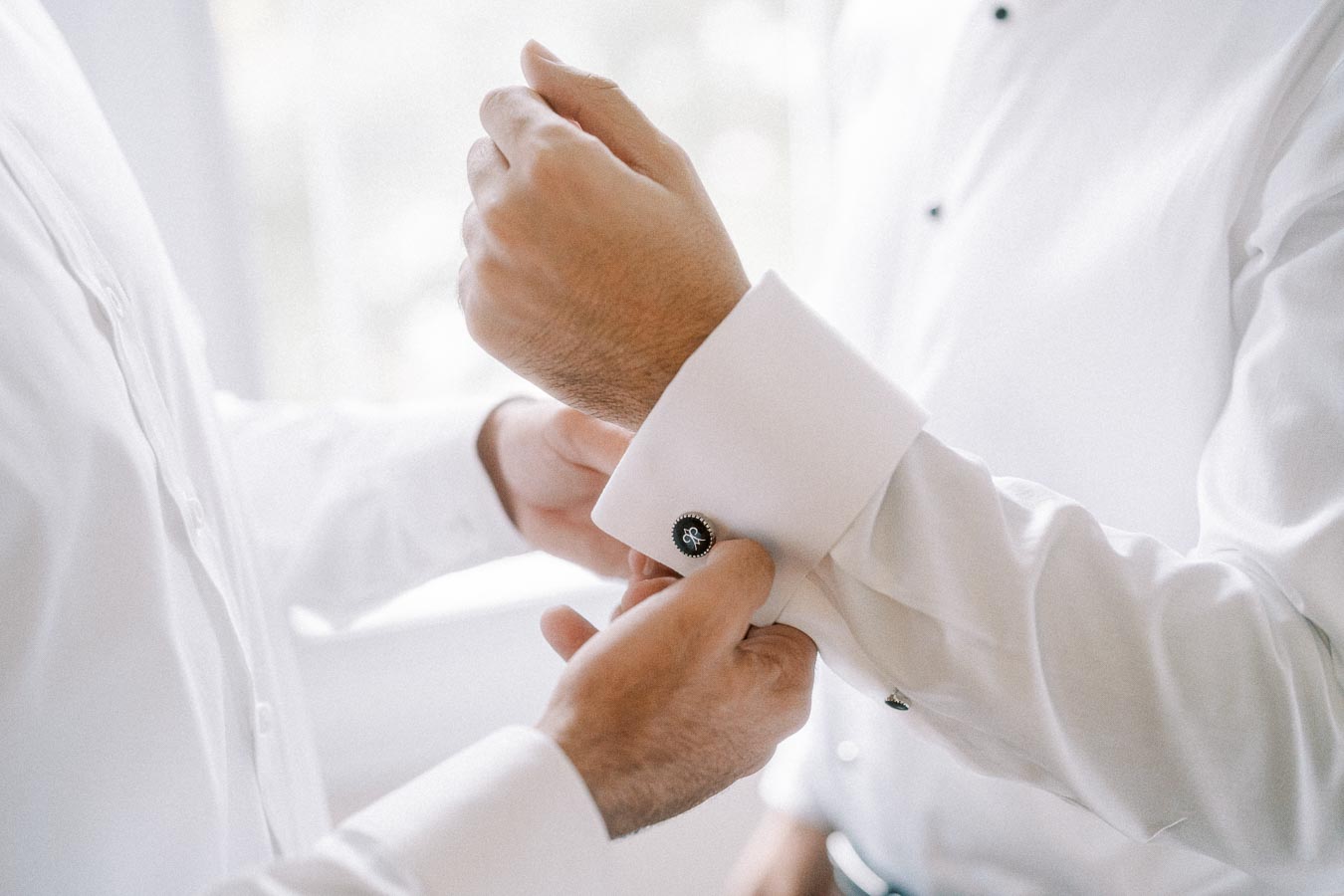 Formal attire preparation: Close-up of a person adjusting cufflinks on a white dress shirt, symbolizing elegance and