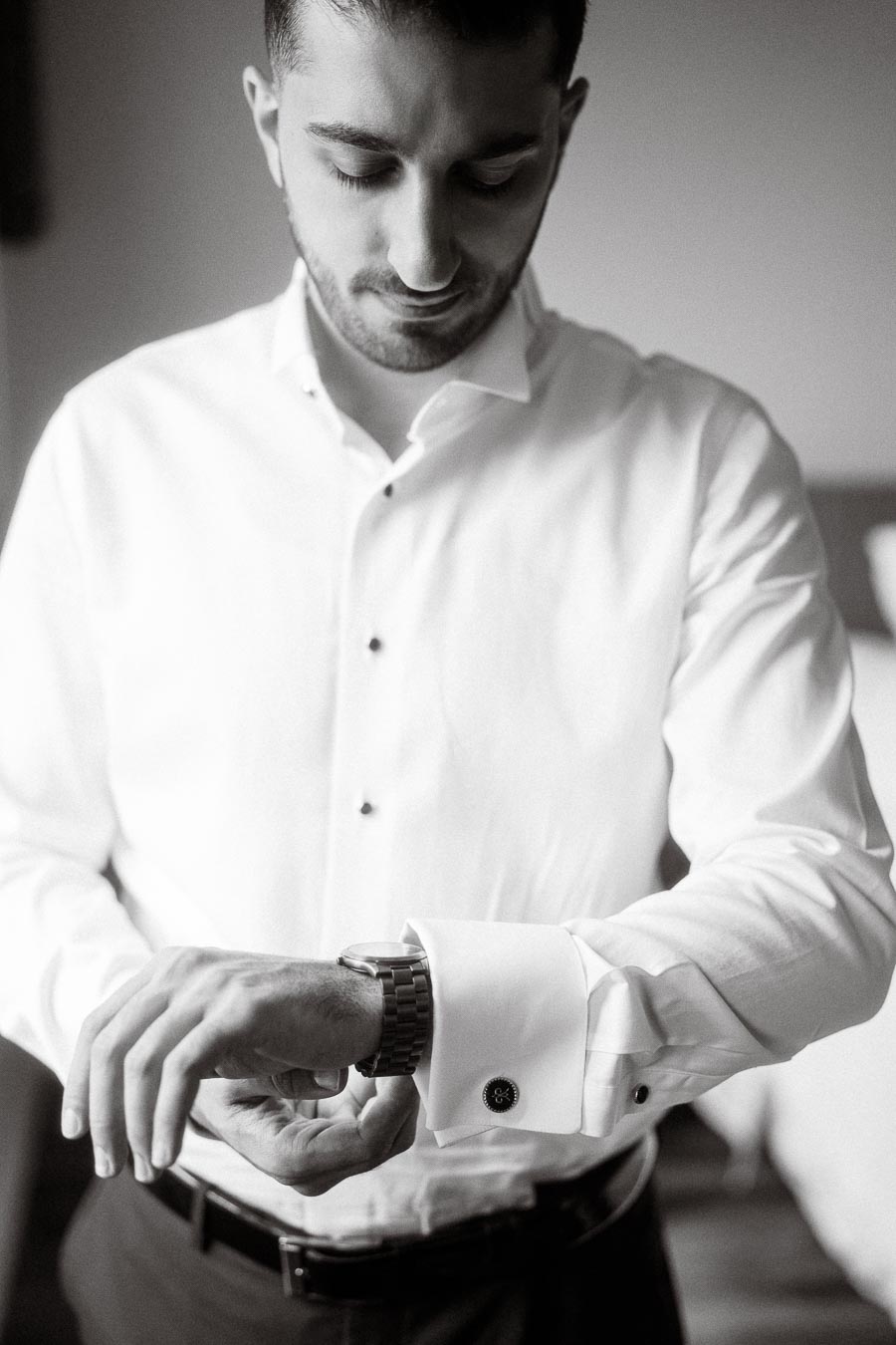 Man adjusting cufflinks on a formal white shirt while checking the time on his wristwatch.