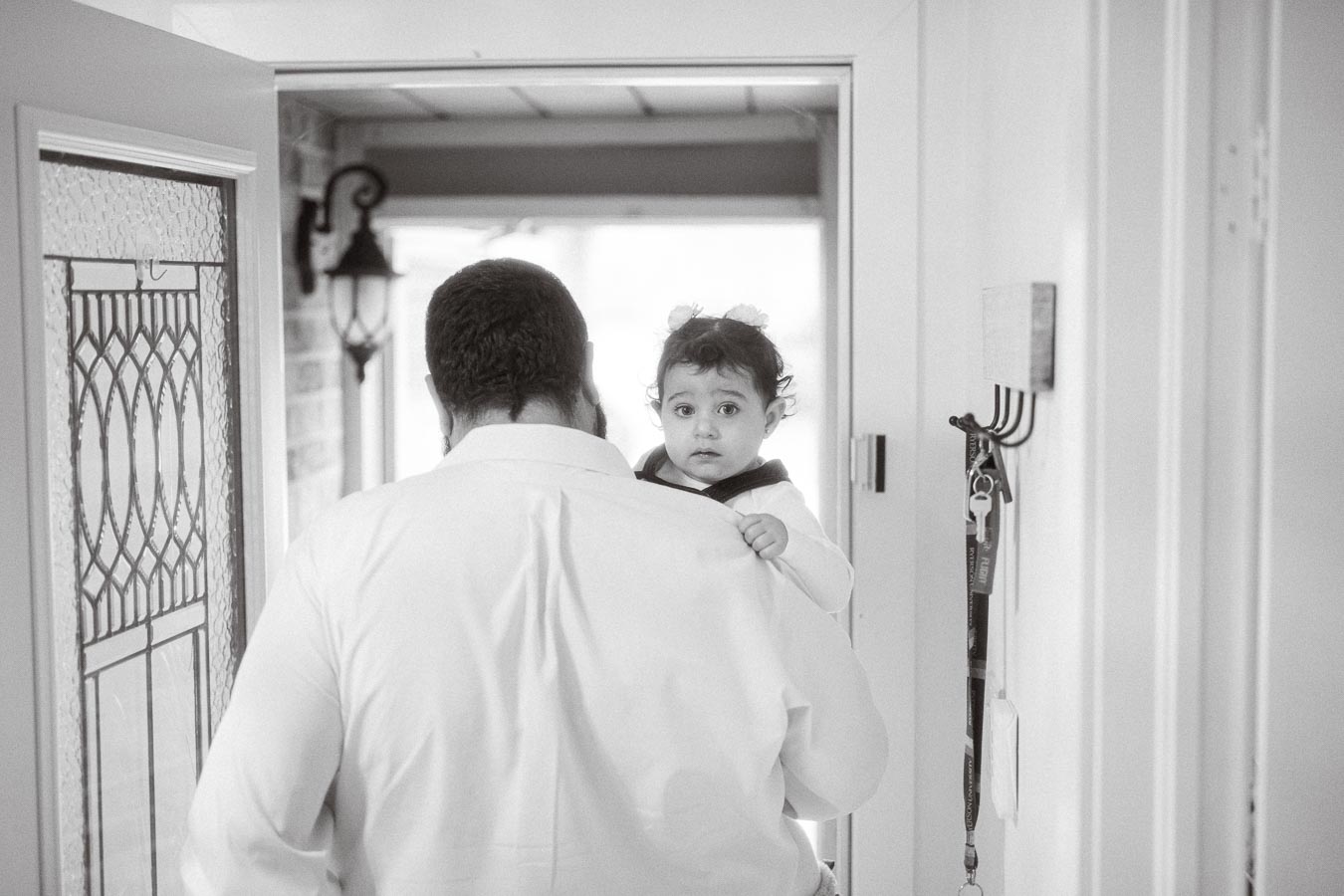 A black and white photo of a man carrying a toddler on his shoulder while standing in a doorway, with the child looking into