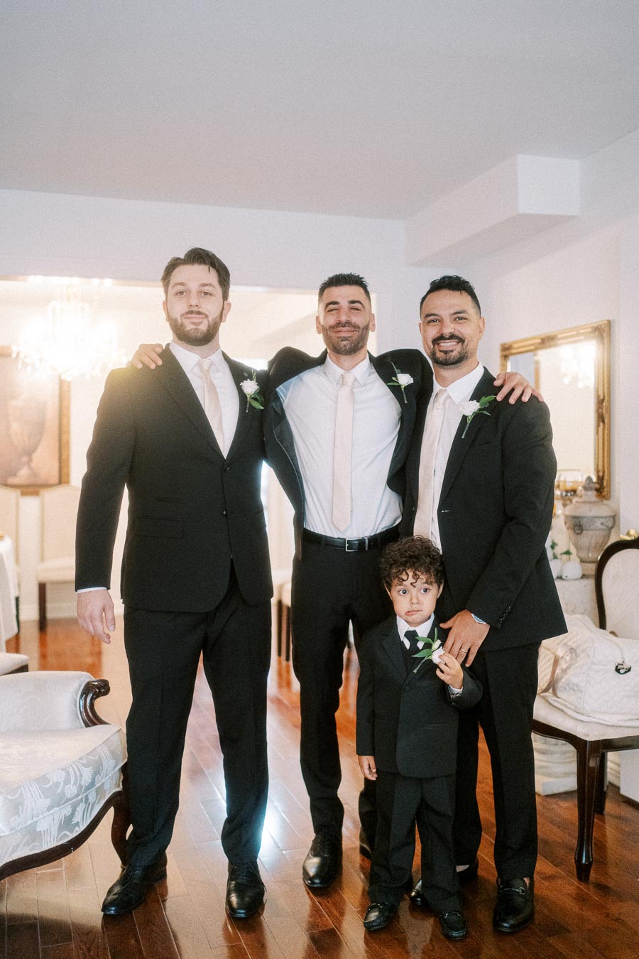 A group of men and a boy in matching formal attire pose together indoors, highlighting a special occasion with smiles and