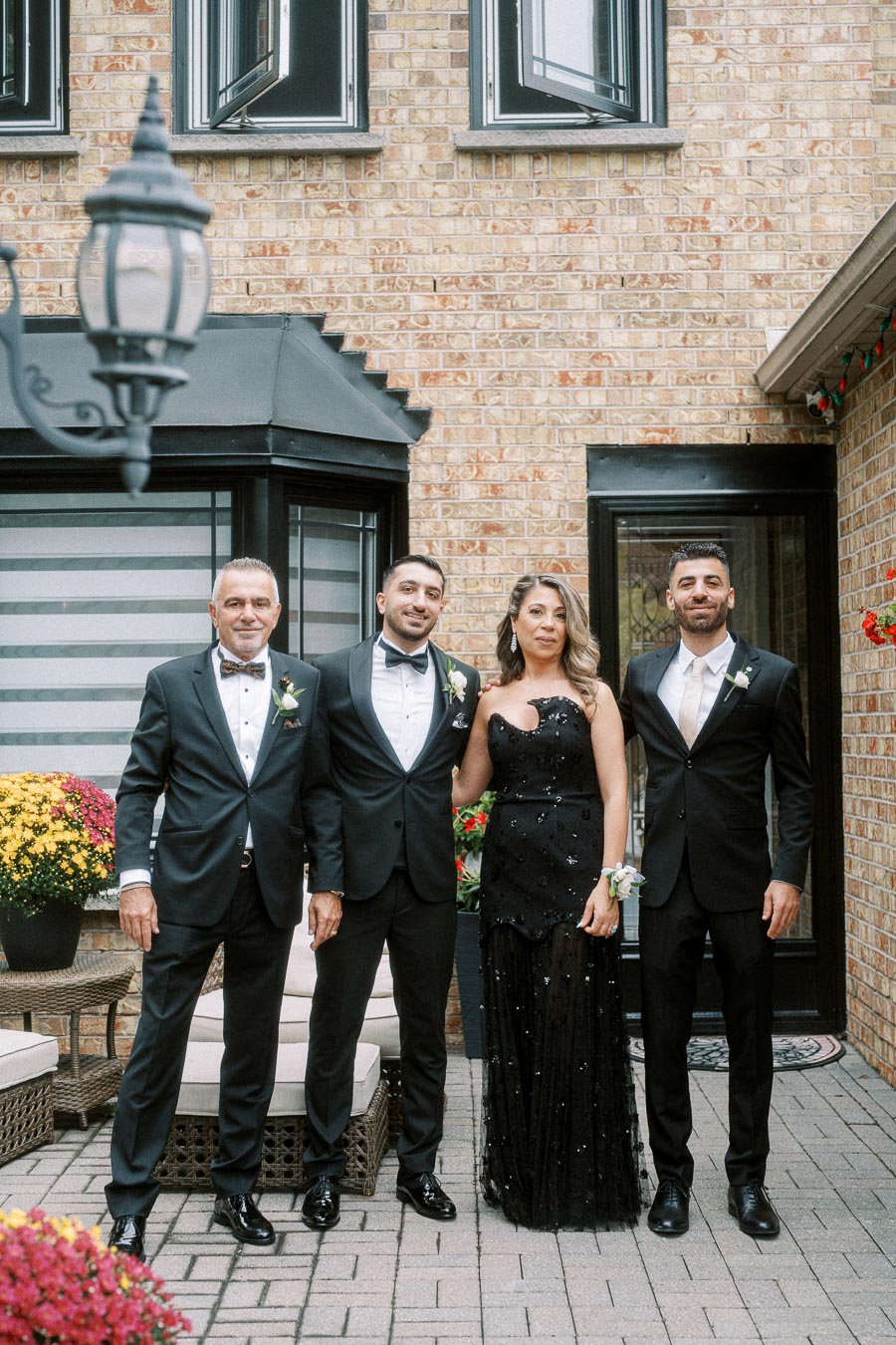 A group of four people dressed in formal black attire posing outside a brick building with decorative windows, surrounded by
