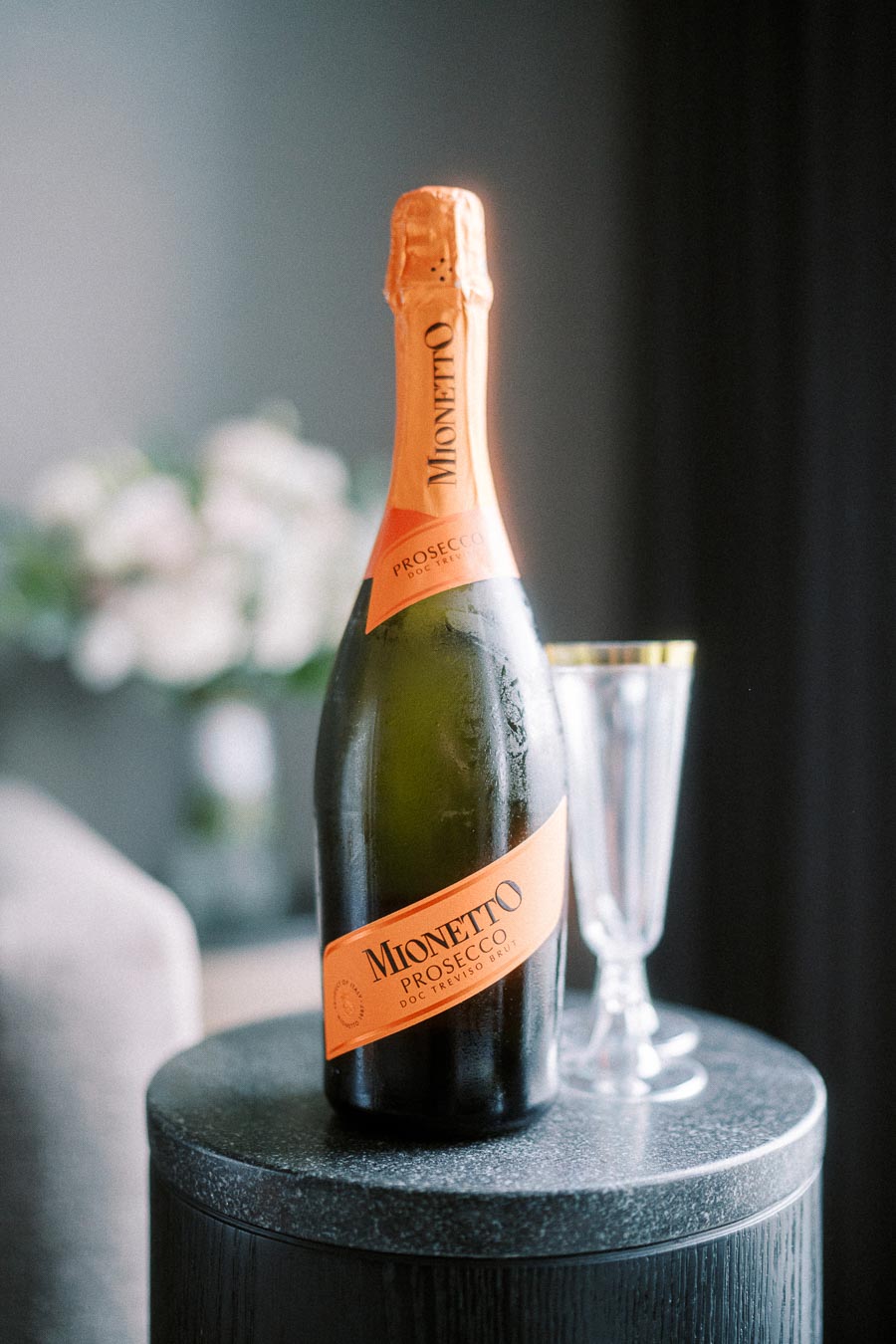 Bottle of Mionetto Prosecco on a table with a sparkling wine glass, elegant indoor setting.