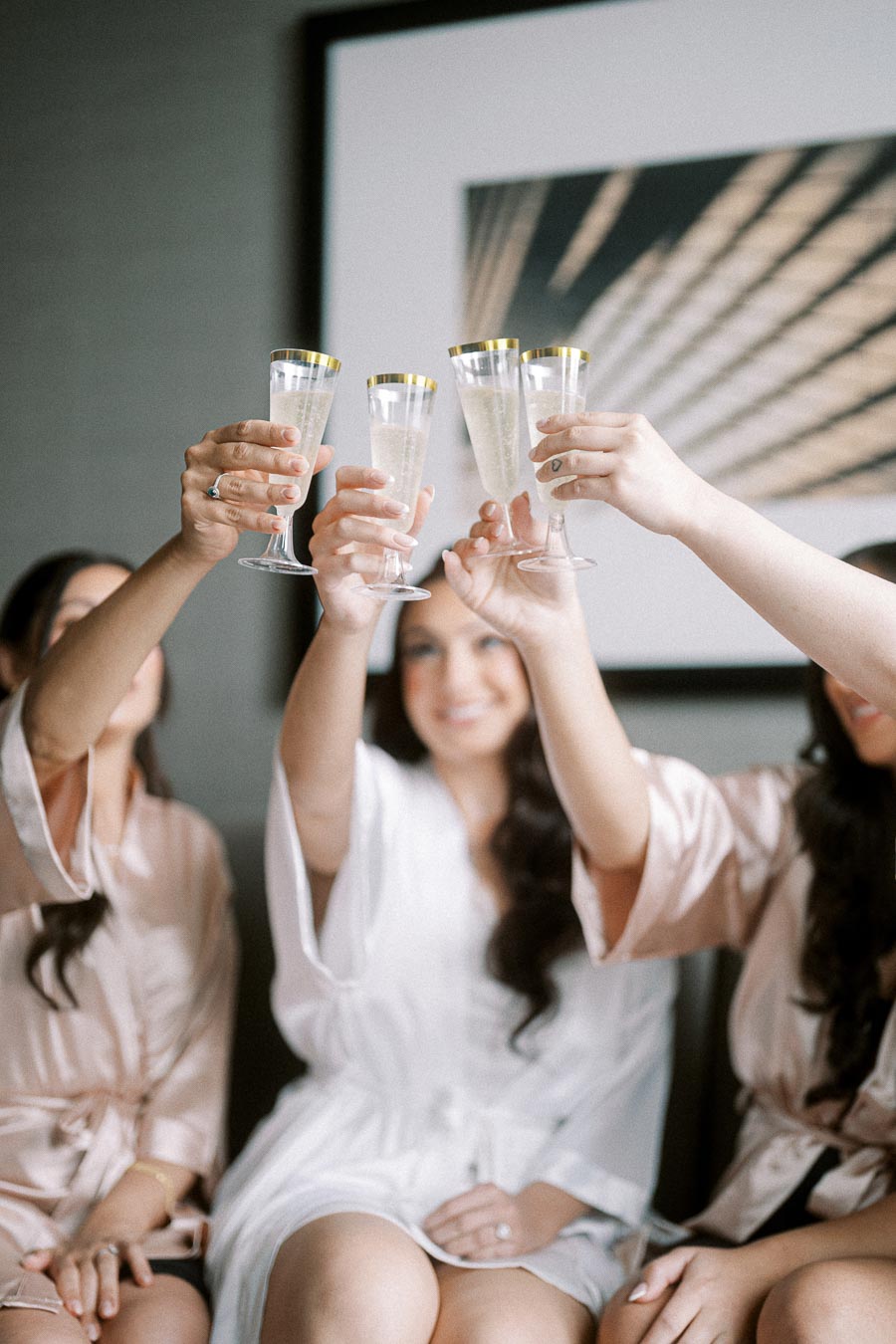 Bridesmaids wearing silk robes toasting with champagne glasses, celebrating a special moment together before a wedding.