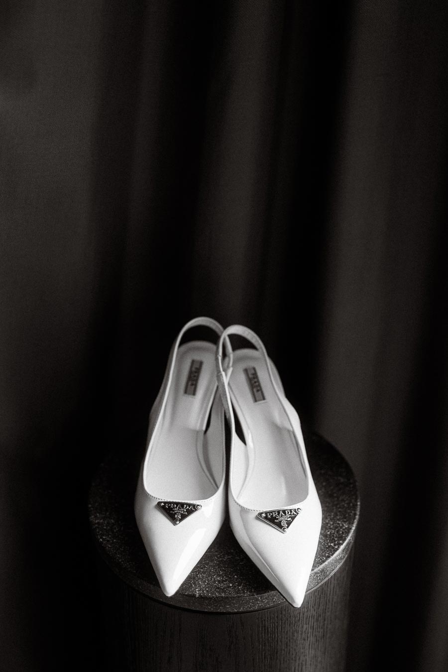 Elegant pair of white pointed-toe high heel shoes with slingback straps, displaying a designer logo, placed on a
