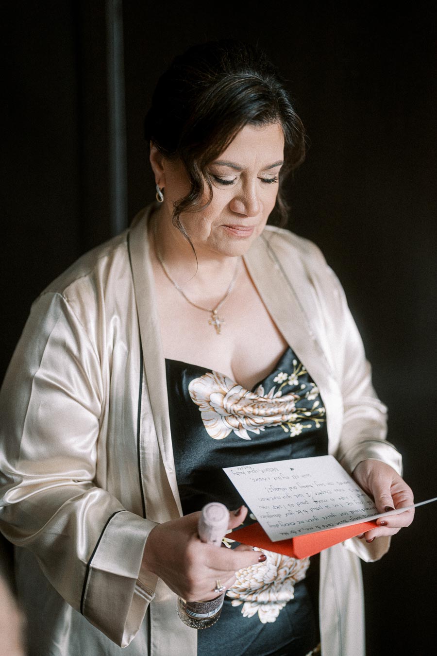 Middle-aged woman in an elegant robe reading a handwritten letter, holding a small bottle, thoughtful expression.