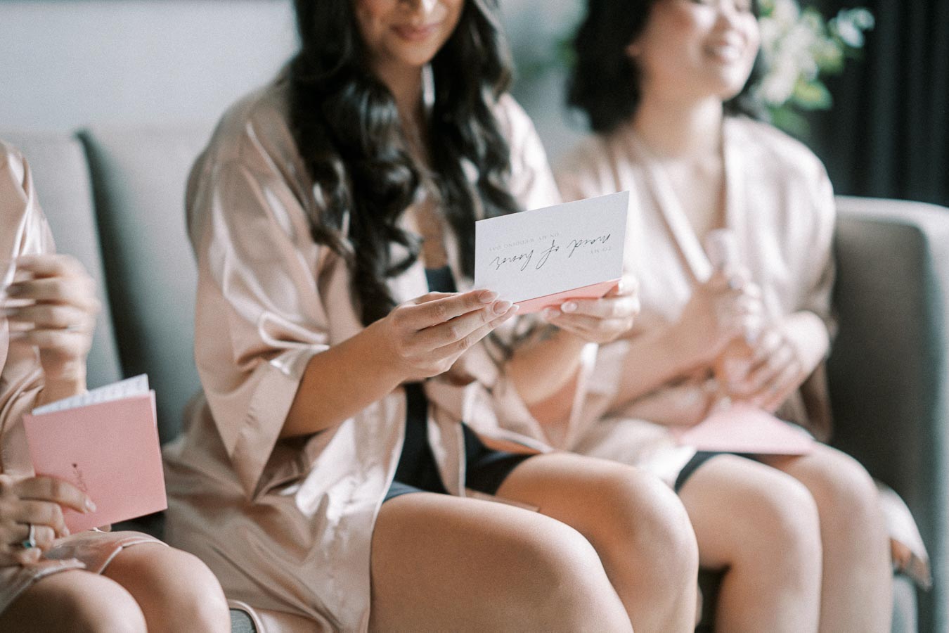 Women in silk robes sitting on a couch reading heartfelt cards, preparing for a special occasion, conveying friendship and