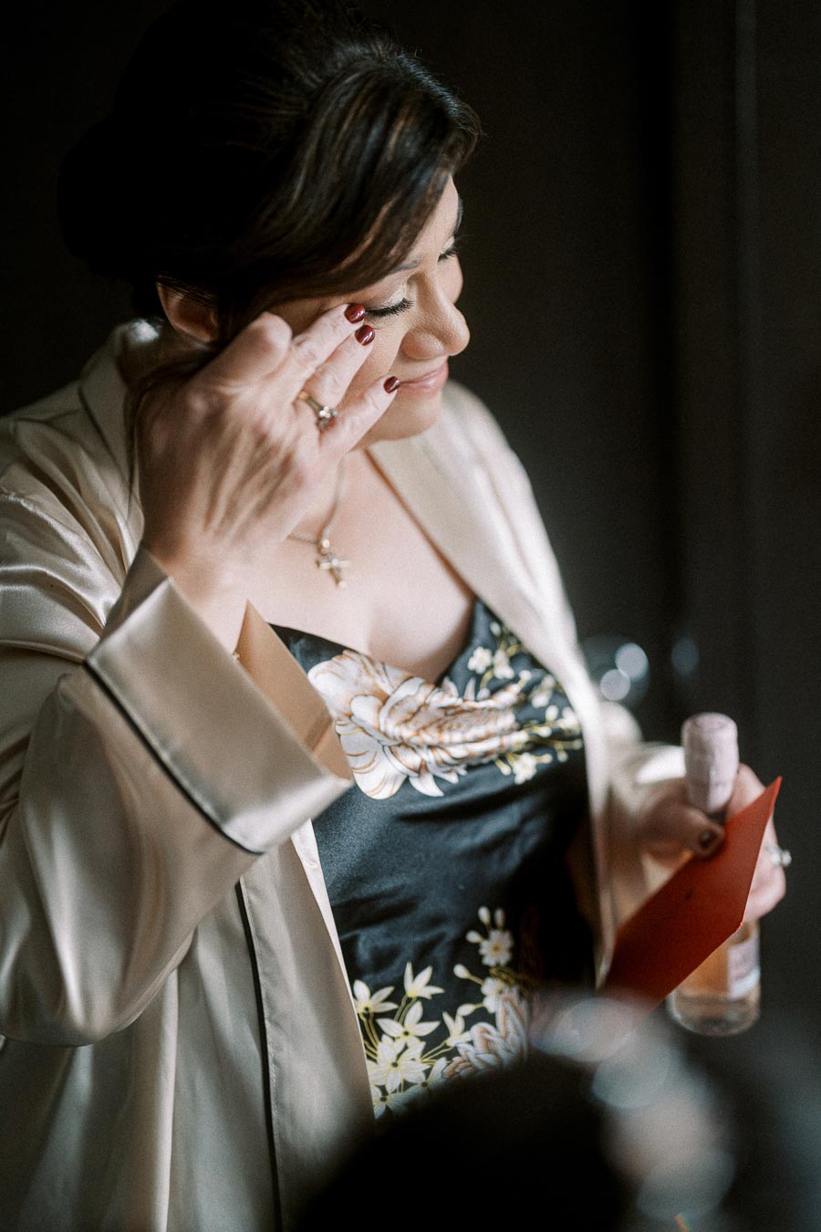 A woman dressed in an elegant floral-patterned robe, thoughtfully wiping a tear from her eye while holding a letter and a