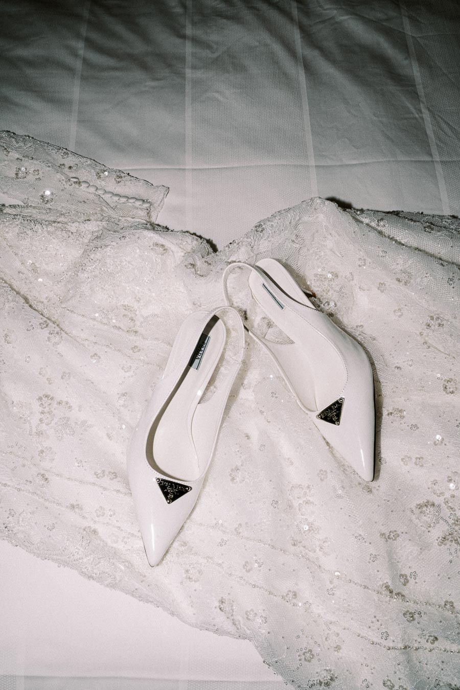 White wedding shoes with silver accents placed on an intricate lace wedding dress with sequins, showcasing elegant bridal