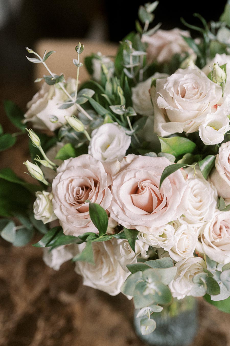 A close-up image of a beautiful flower arrangement featuring soft pink roses and white blossoms, accented with lush green