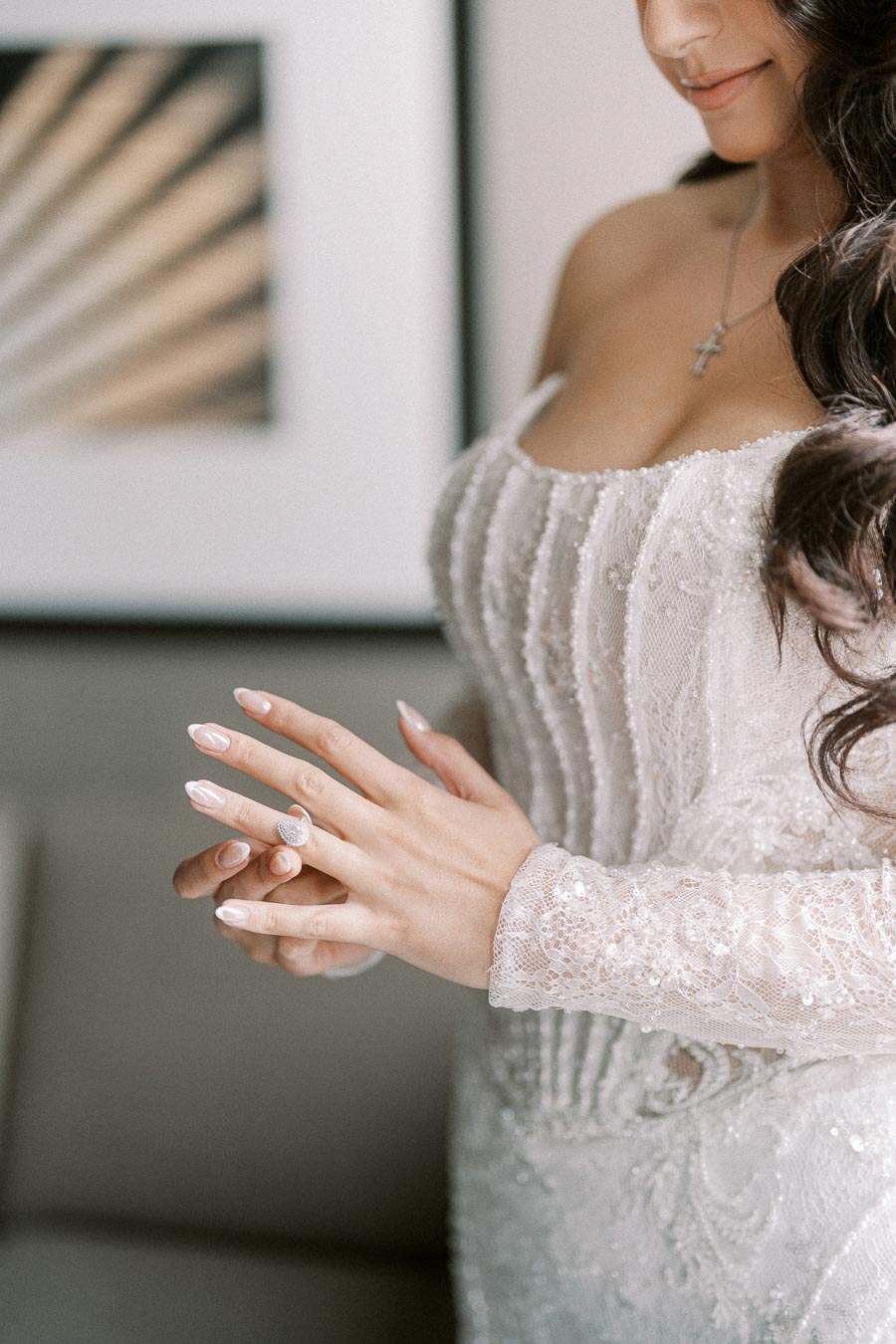 Bride in elegant lace wedding dress with beaded details, showcasing a diamond ring, preparing for her wedding day.