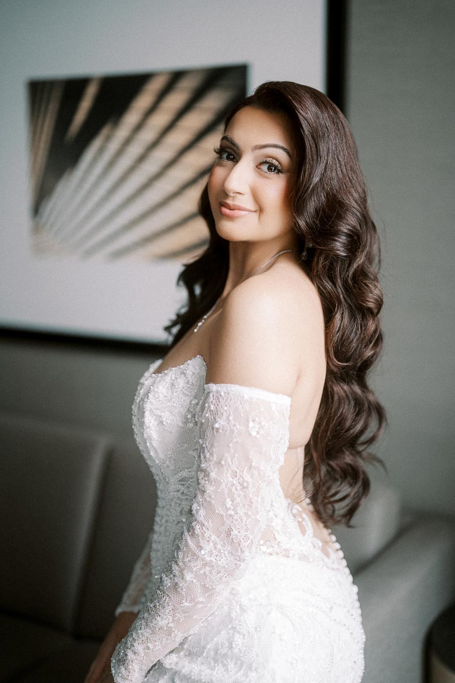 A woman in a white lace off-shoulder wedding dress with long, wavy hair.