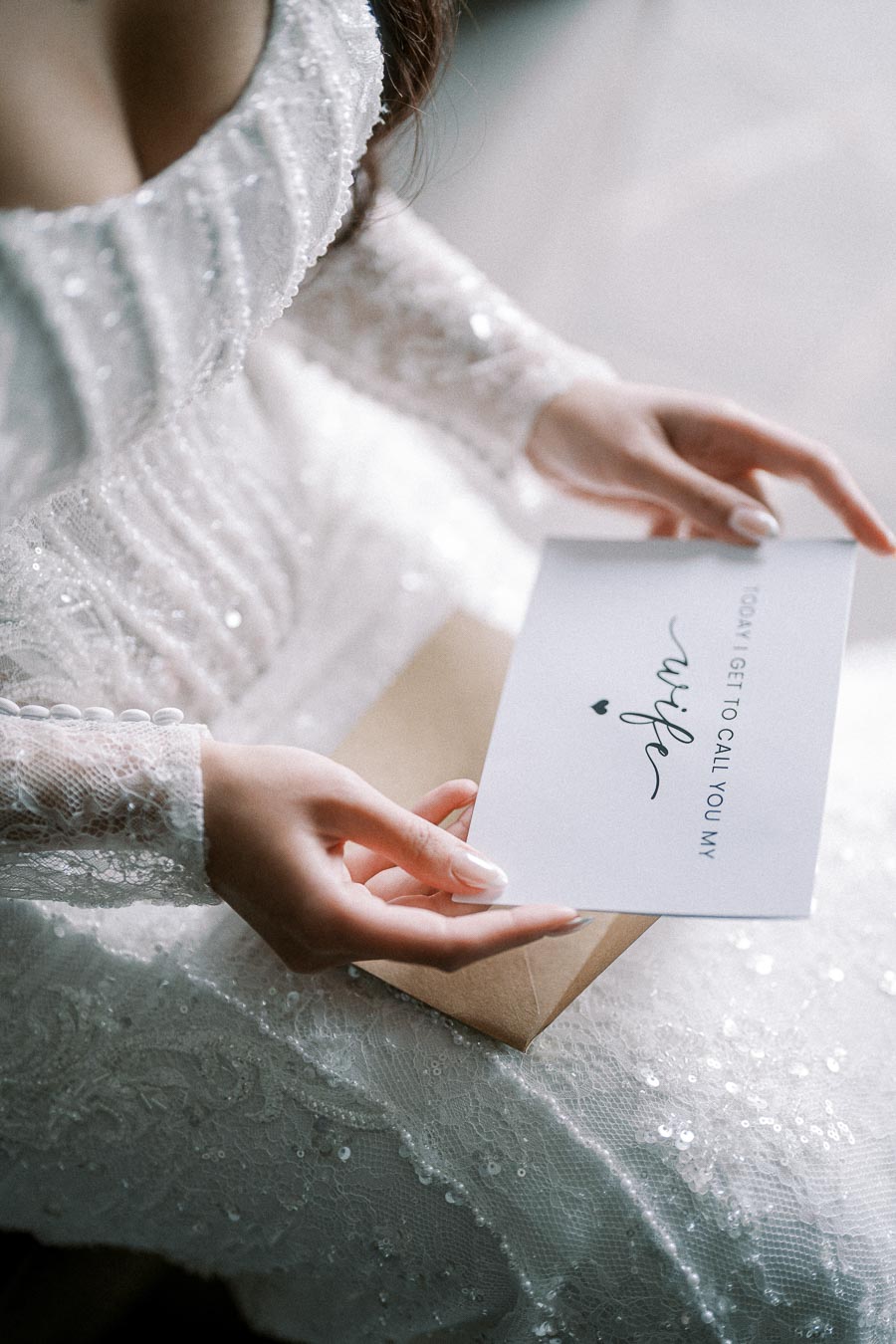 A bride in a lace wedding dress holding a card with the text Today I get to call you my wife.