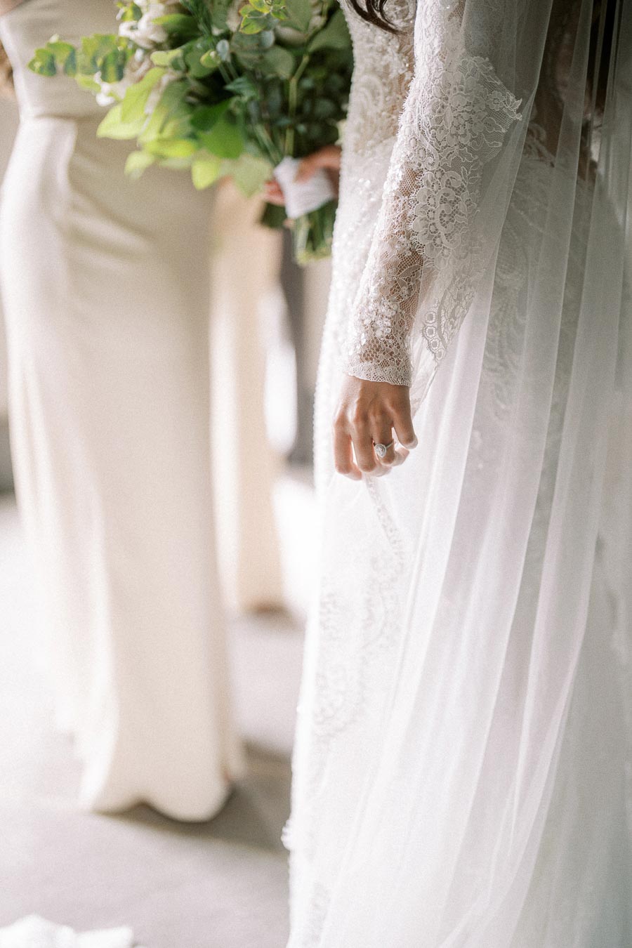 Elegant bride holding a bouquet, showcasing intricate lace detailing on her wedding dress and a delicate ring on her finger.