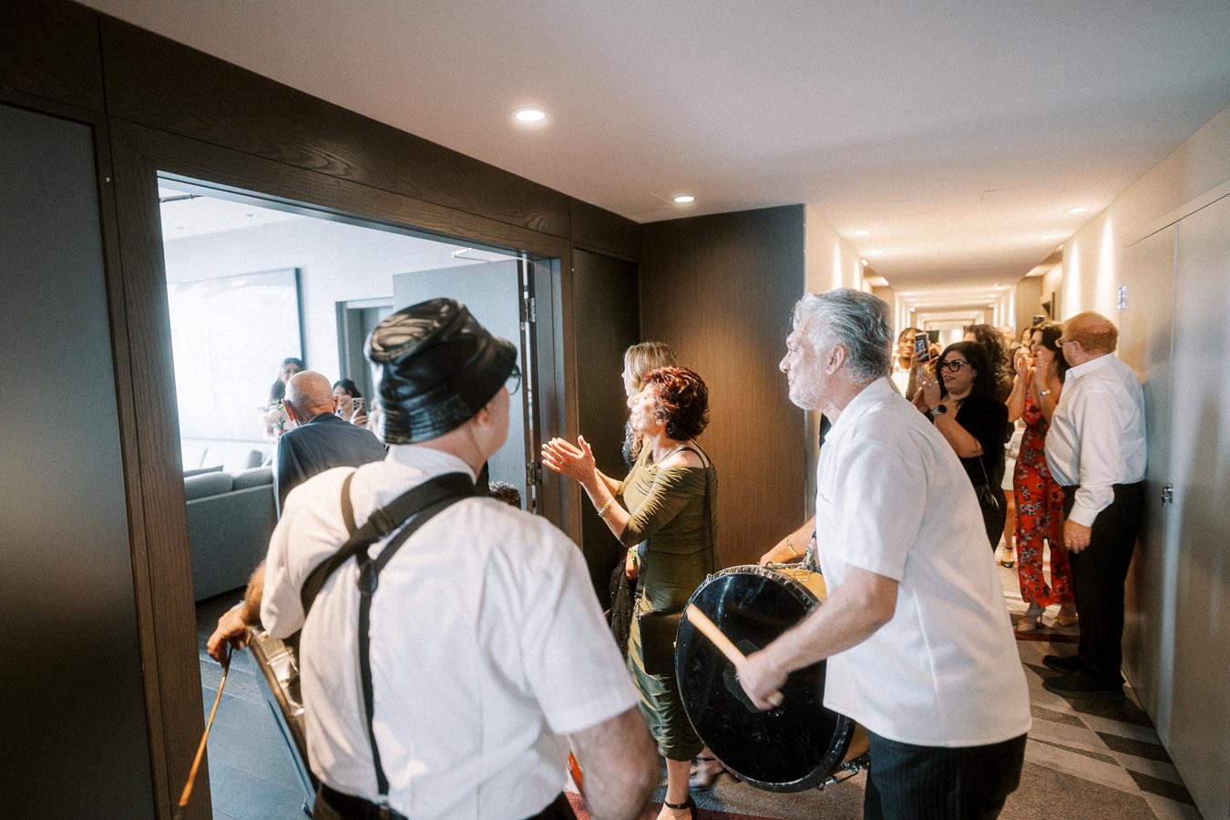 A group of people celebrating indoors with musicians playing drums in a lively hallway atmosphere.
