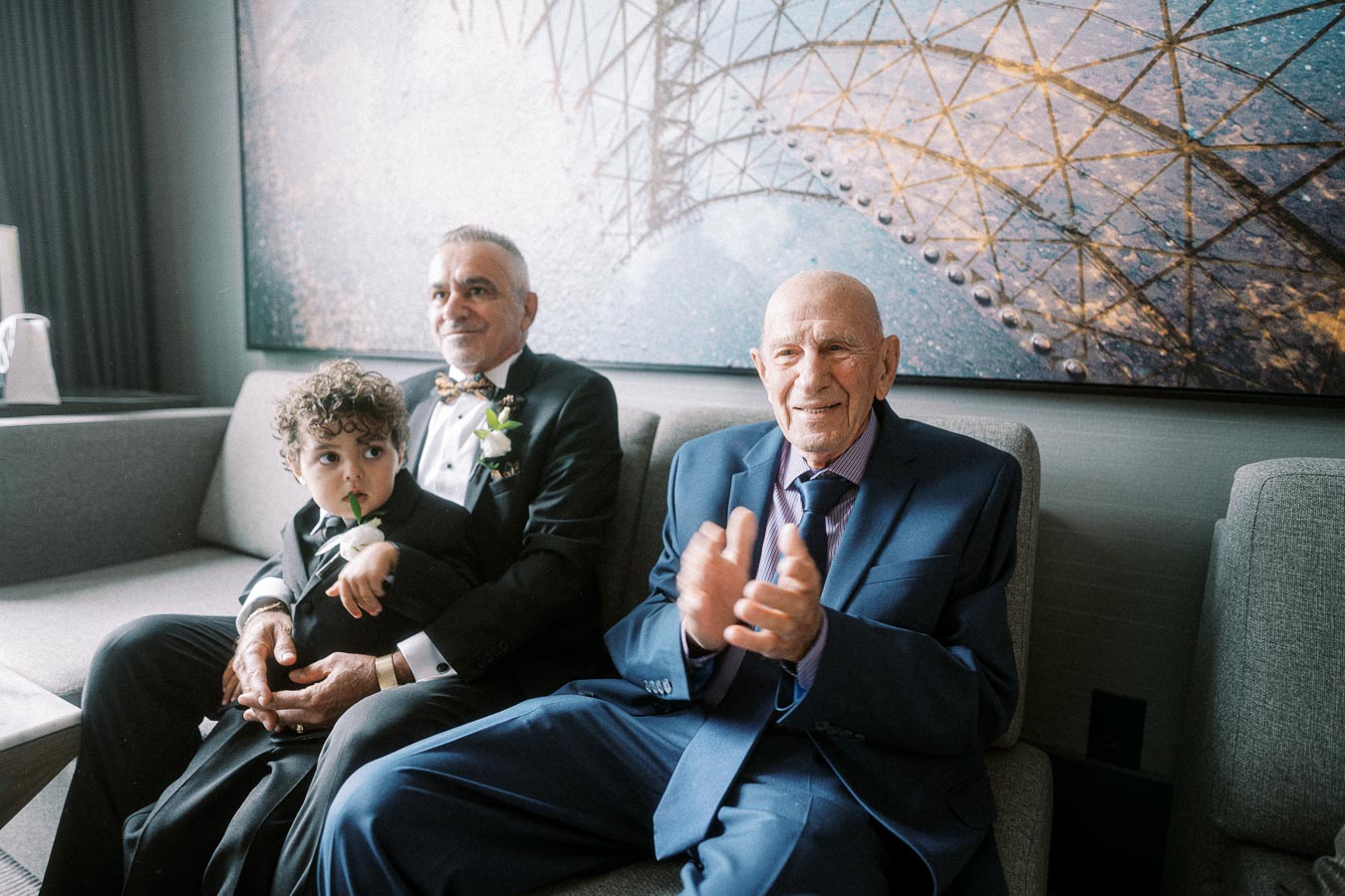 Three generations of a family in formal wear sitting together, featuring a child with curly hair, a middle-aged man with a