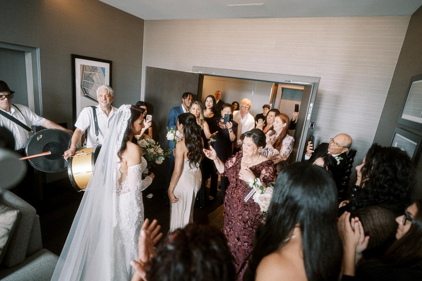 A joyful indoor wedding celebration featuring a bride in a white gown and veil, surrounded by family and friends capturing
