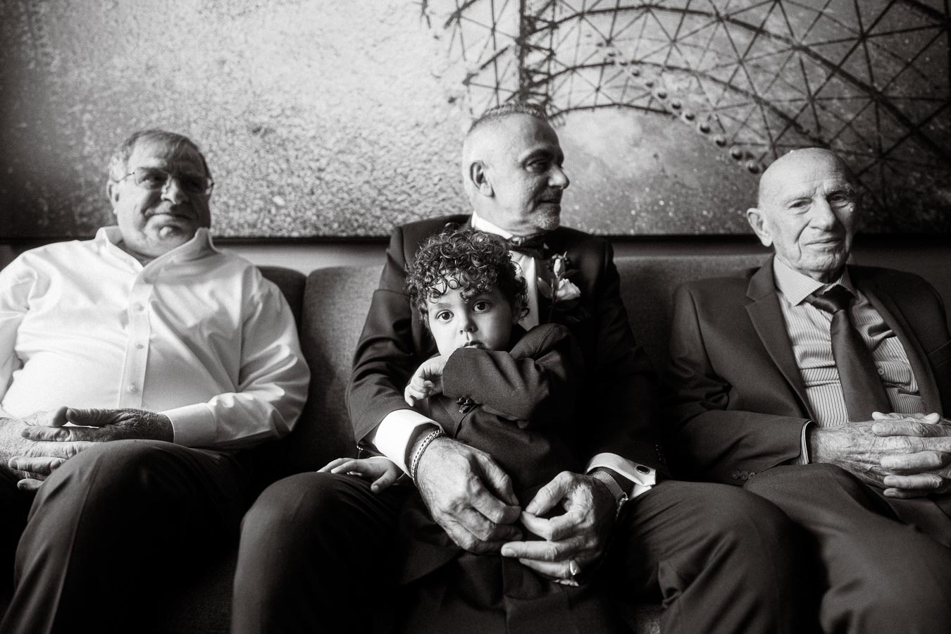 Black and white image of three elderly men and a young child seated on a couch, highlighting generational connections and