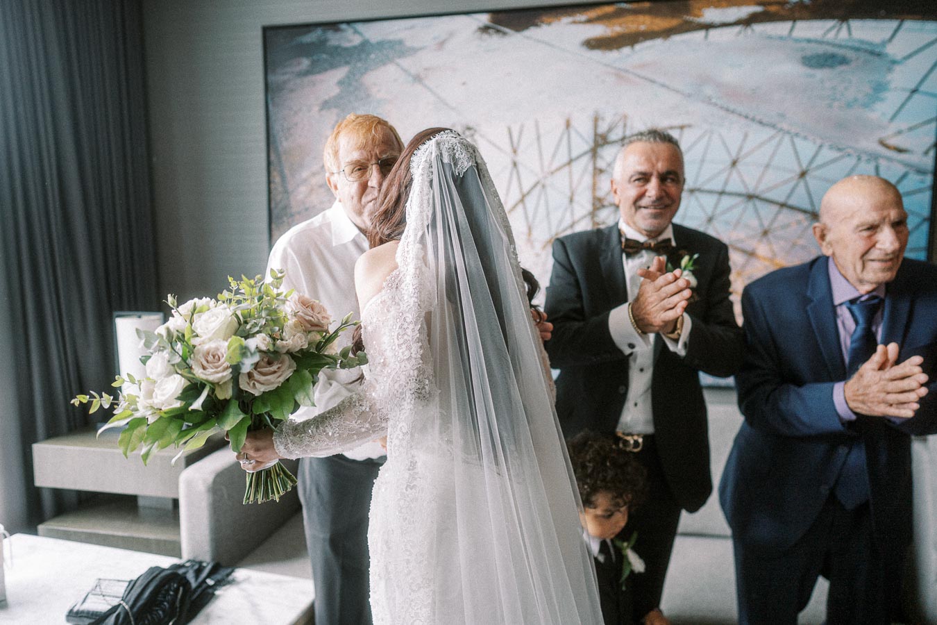 A bride in a white lace wedding gown and veil shares a touching moment with an older man, while holding a bouquet of blush