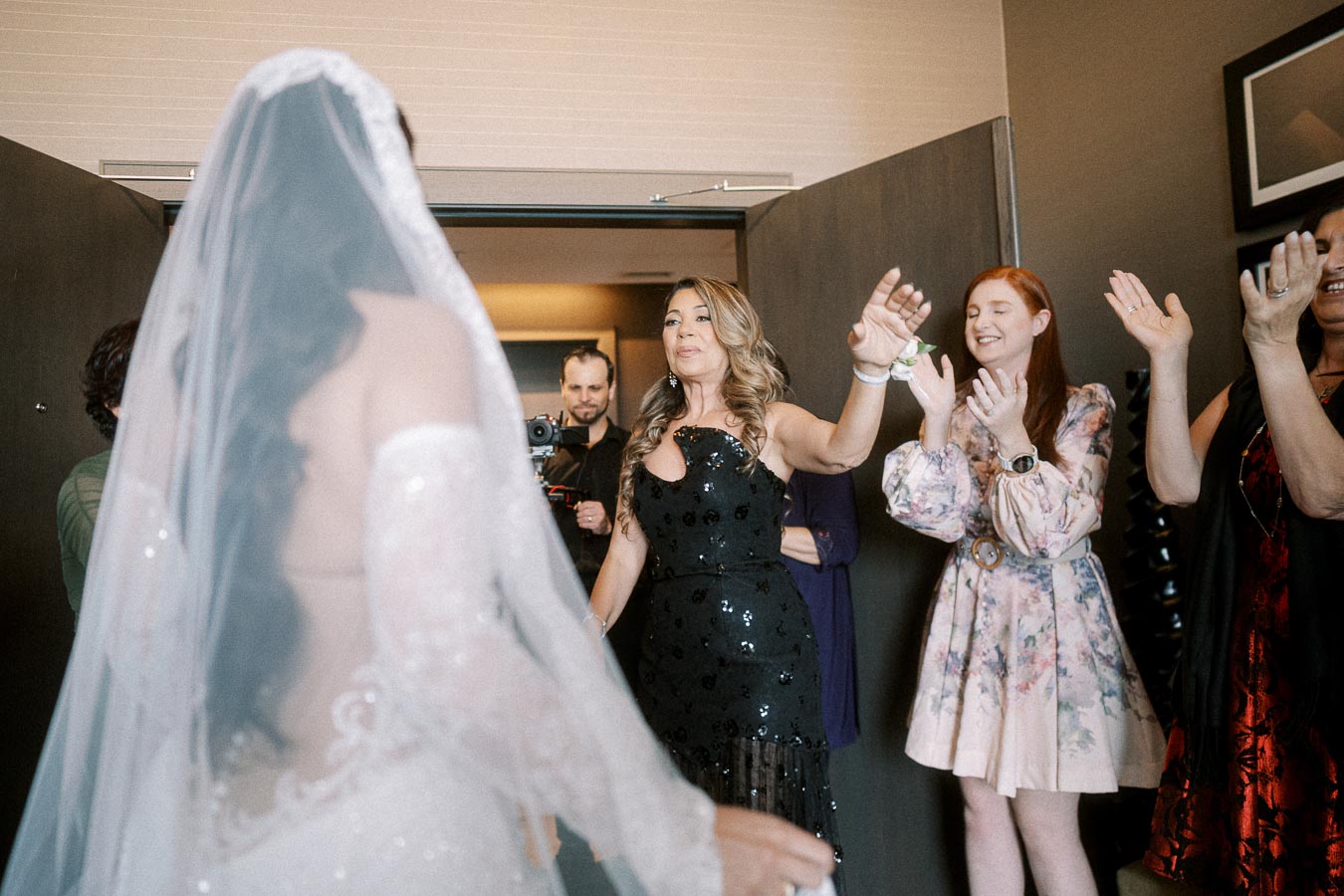 Bride in elegant white gown surrounded by excited wedding guests, capturing a joyful pre-ceremony moment.