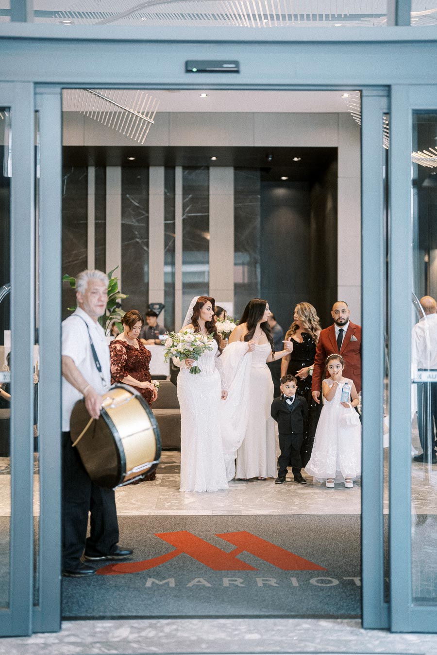 Wedding ceremony at a hotel entrance with a bride holding a bouquet, family members in elegant attire, and a