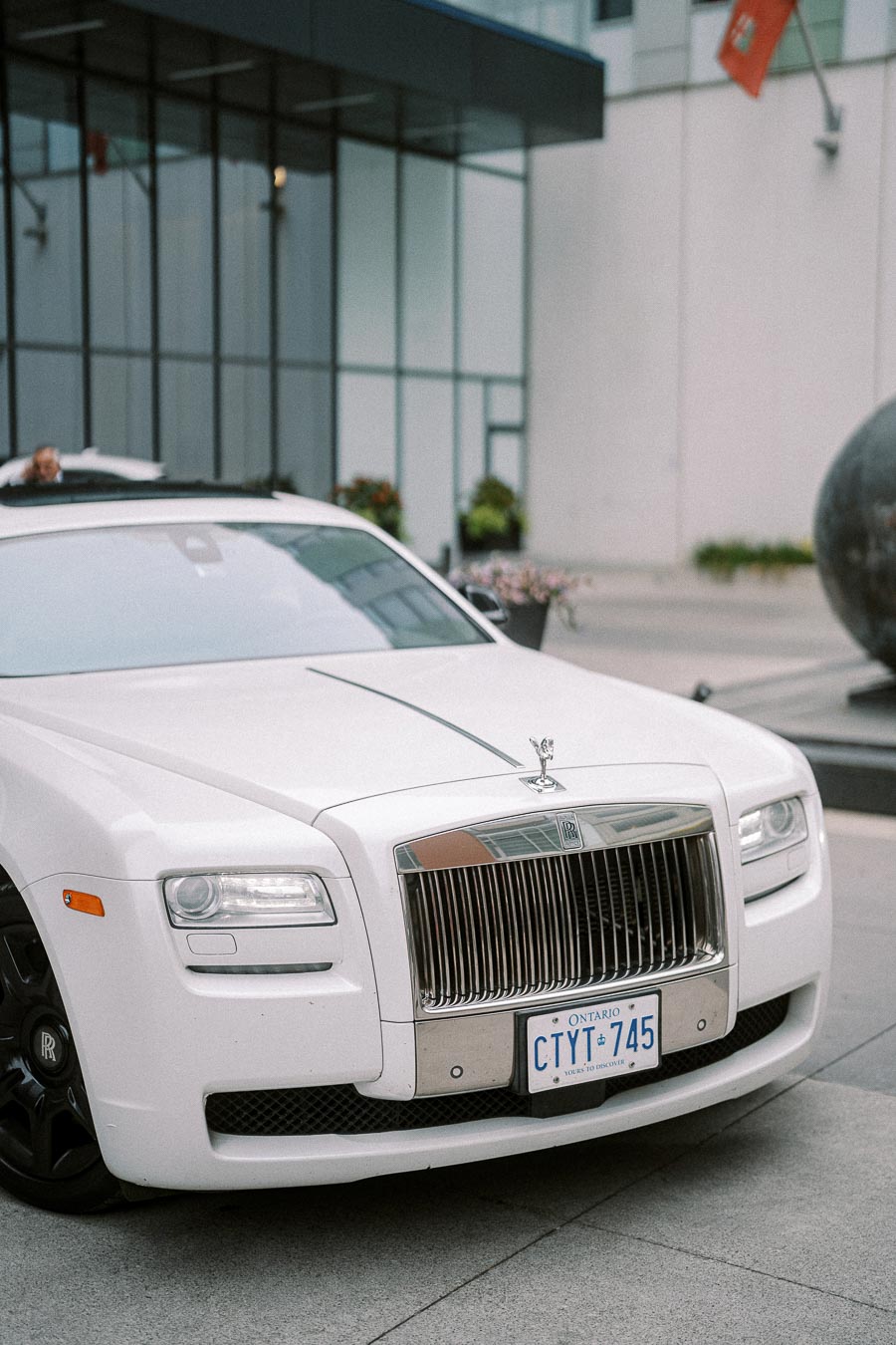 Luxury white Rolls-Royce parked outside a modern building with glass windows, featuring Ontario license plates.
