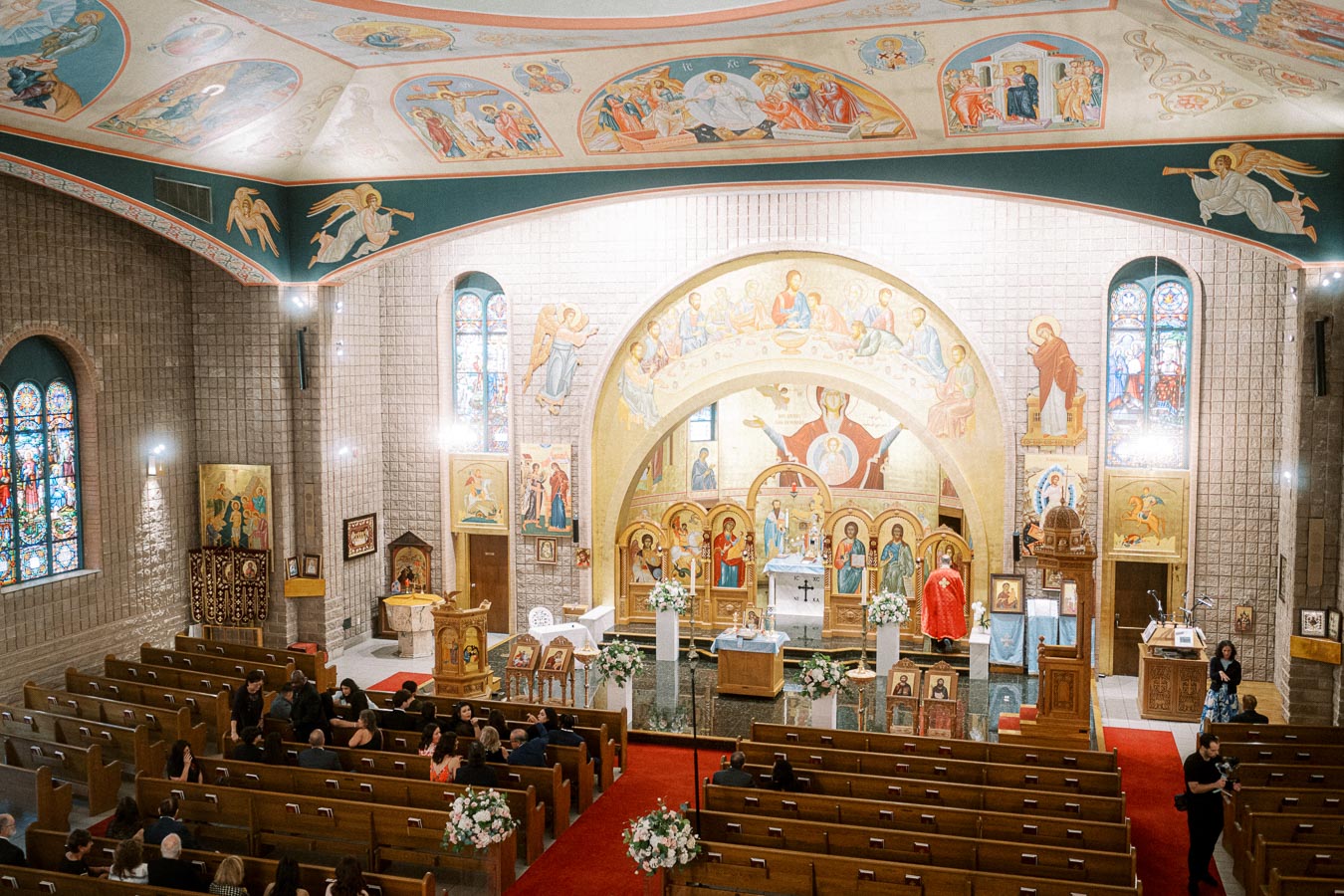 Interior of an ornate Orthodox church featuring detailed religious iconography on the walls and ceiling, stained glass