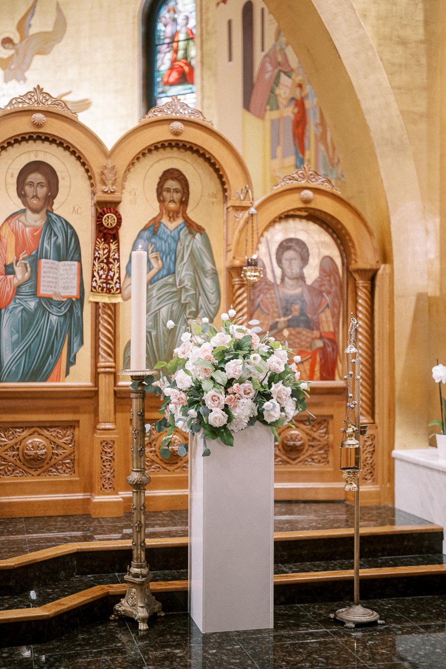 Ornate church altar with religious icons and a floral arrangement in the foreground, featuring pink and white flowers, set