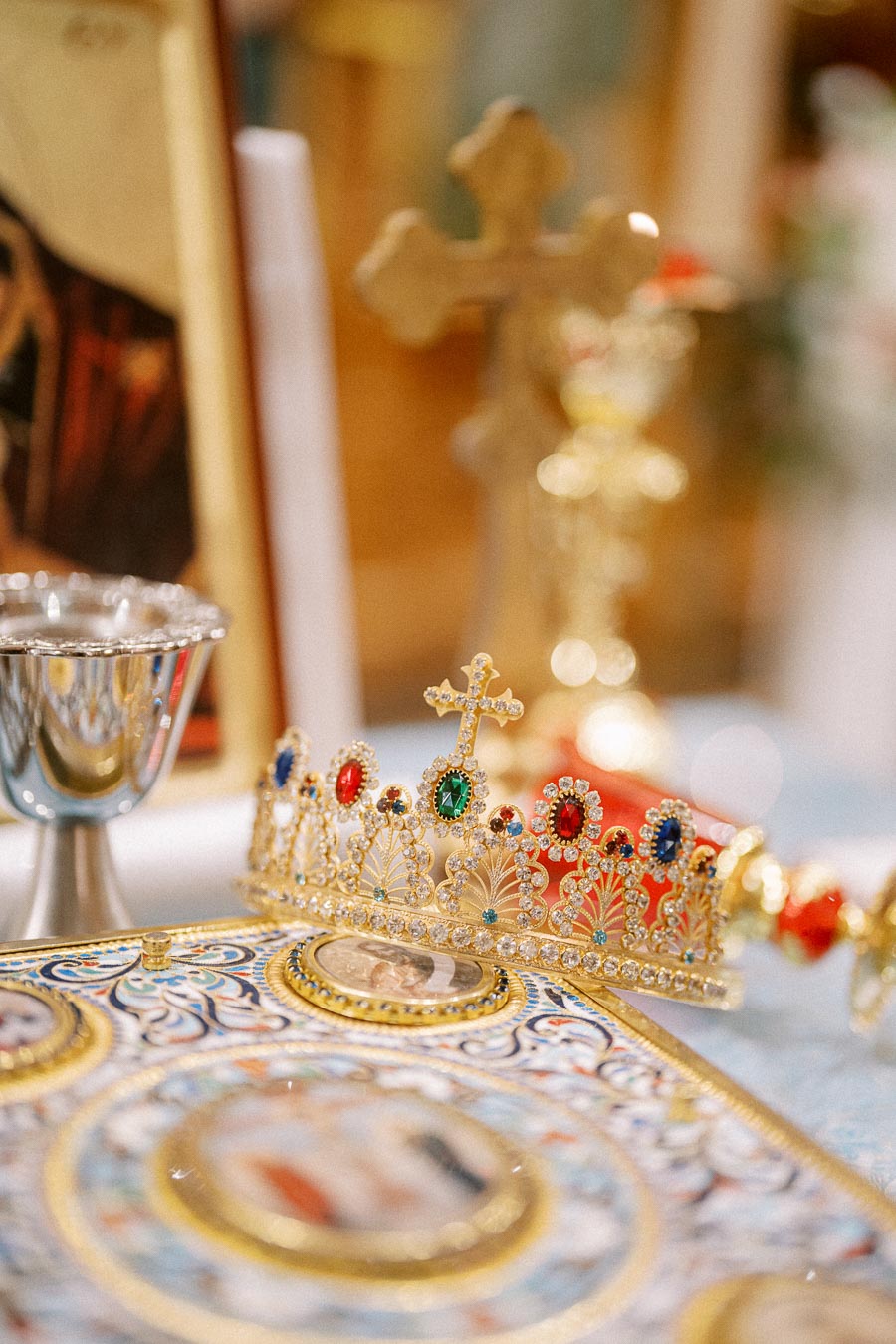 A gold and jeweled religious crown with a cross on top placed on an ornately decorated religious book, accompanied by a