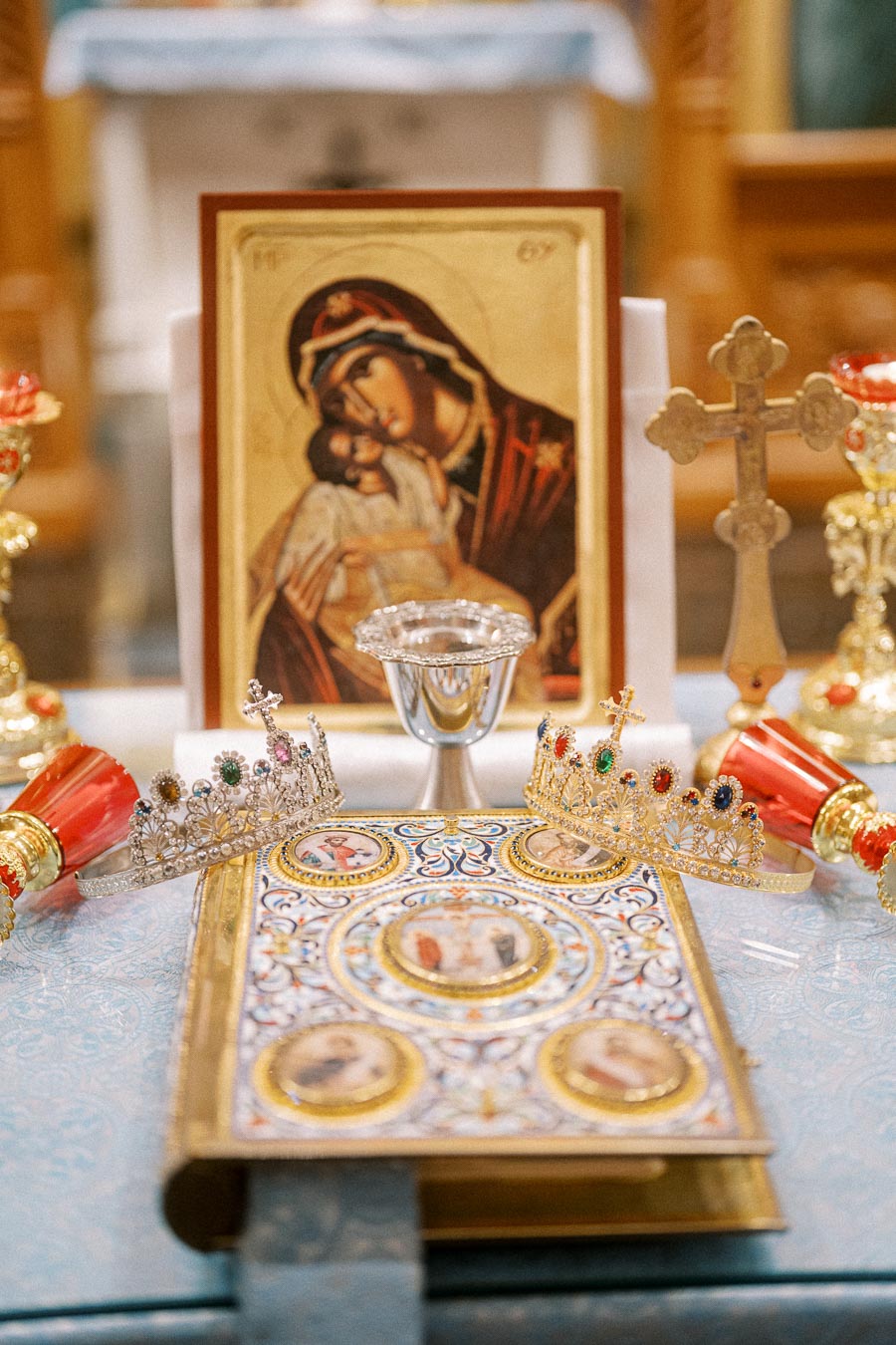 Orthodox Christian wedding ceremony items including an icon of the Virgin Mary, a silver chalice, golden crowns adorned with