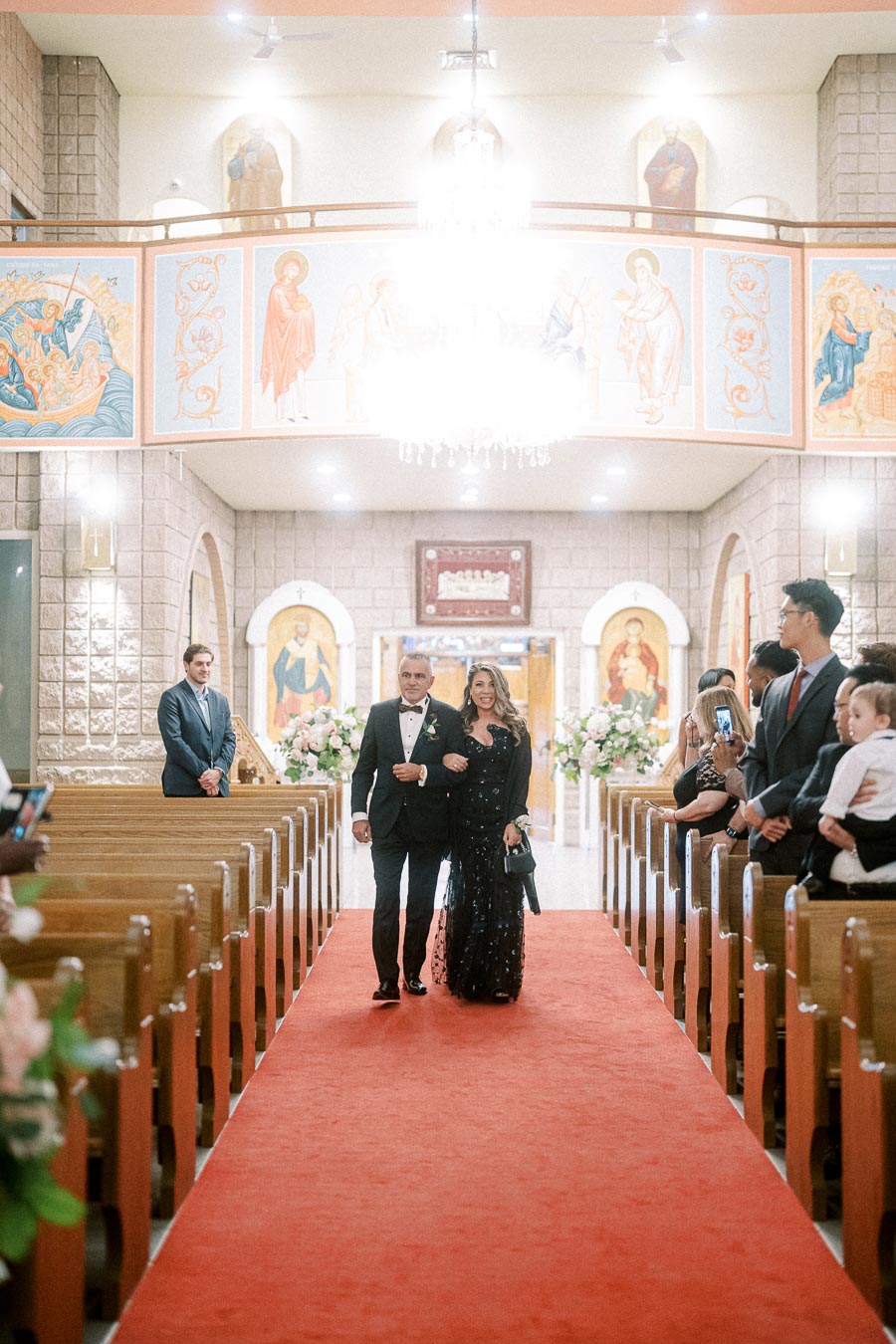 Elegant wedding ceremony in a beautifully decorated church, featuring a couple walking down the aisle on a red carpet with